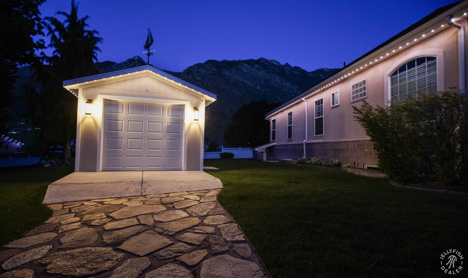 White lights illuminating a detached garage and stone walkway.