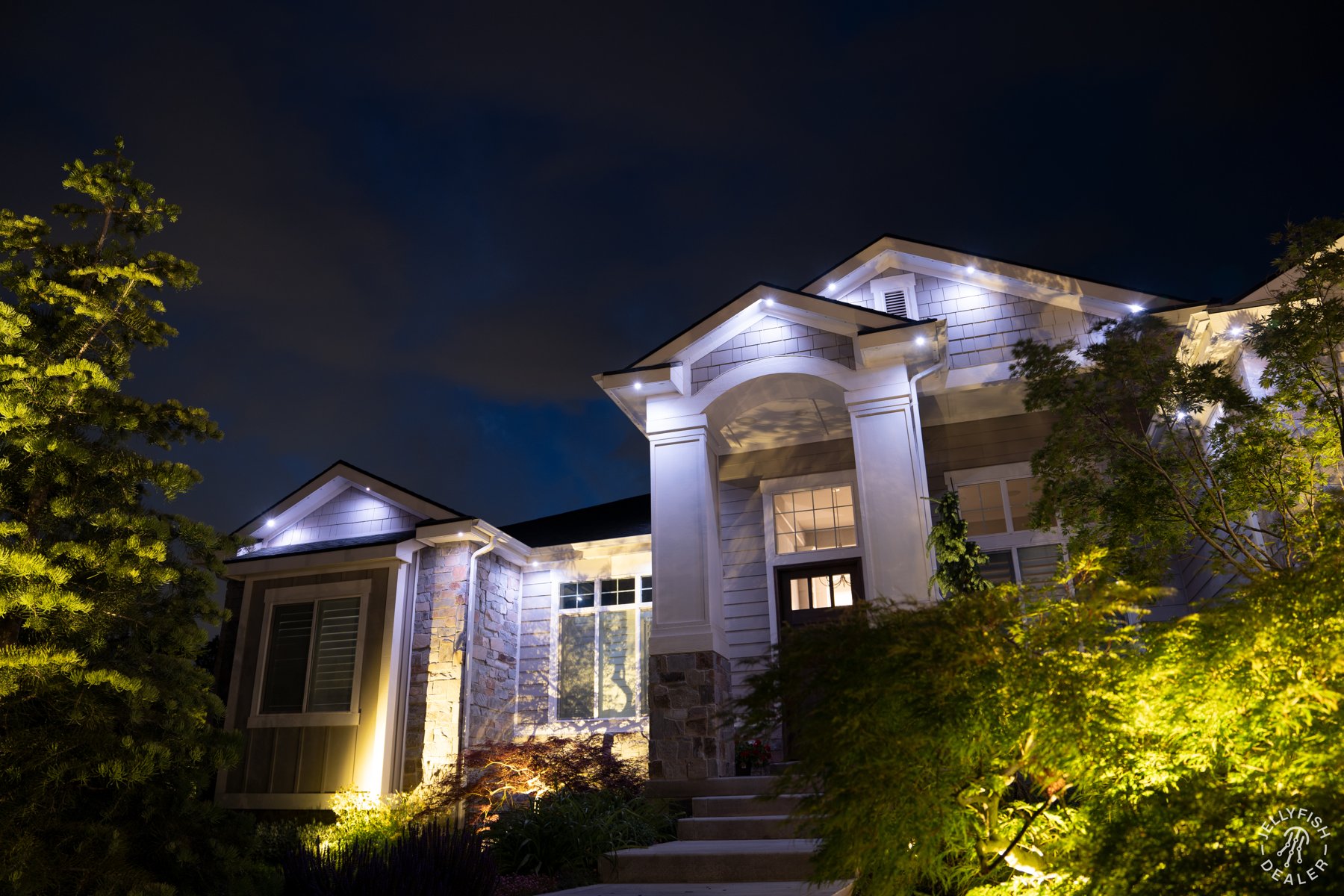 White accent lighting above a columned entry and garden.
