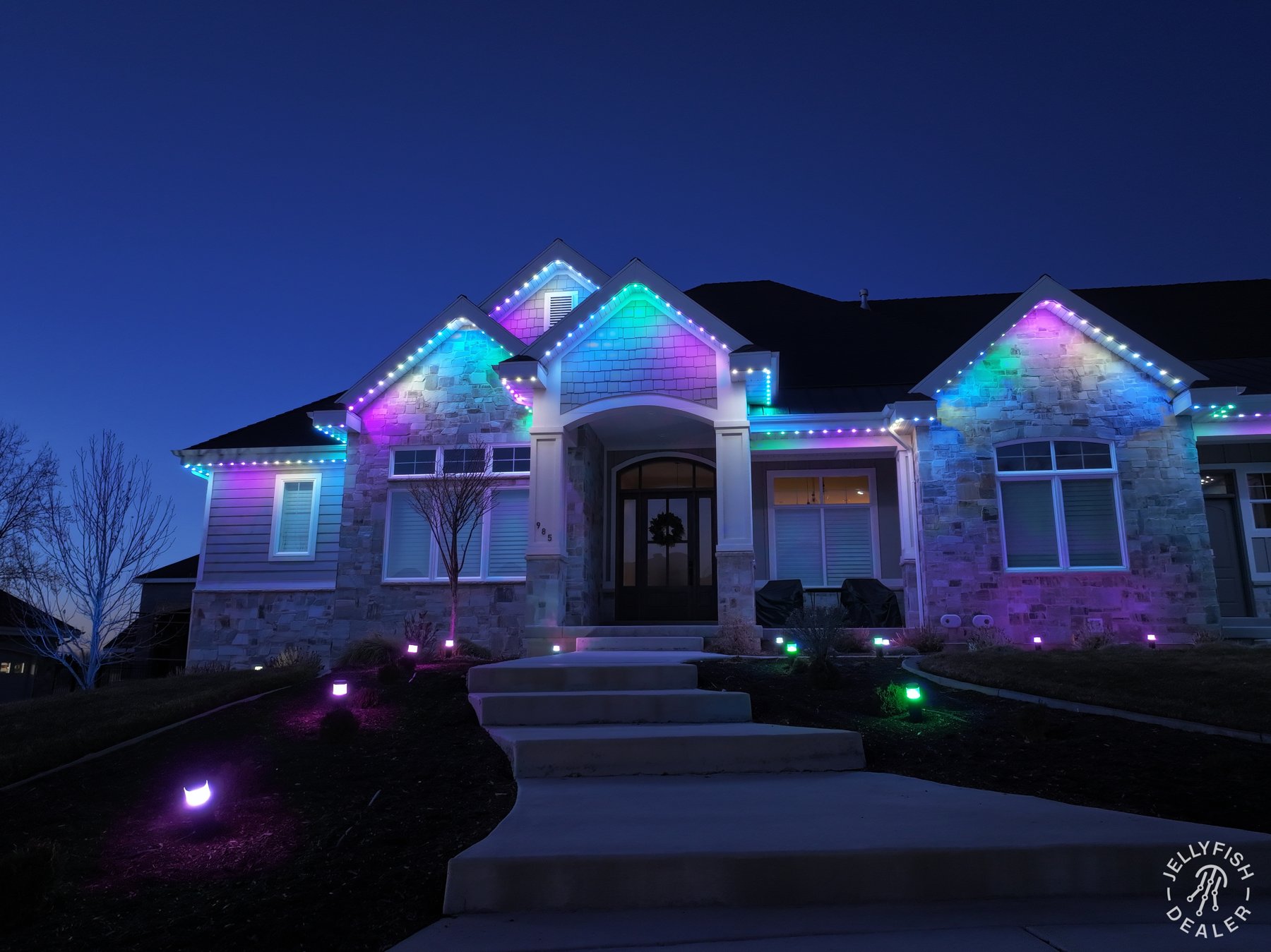 A home with colorful roofline and landscape lighting switched on.