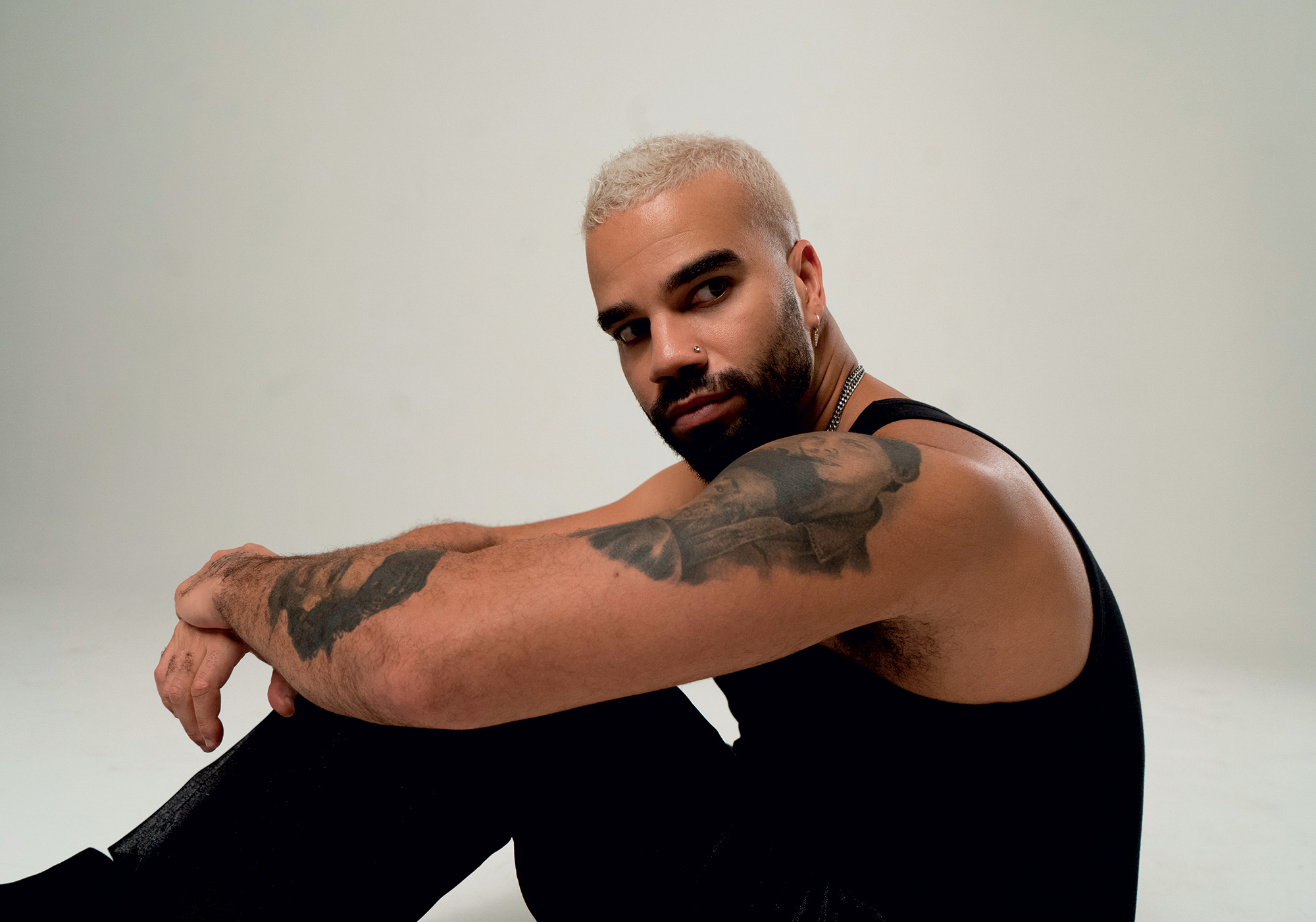 Kállay Saunders seated in a black tank top in a white studio, photographed for Gala Greece