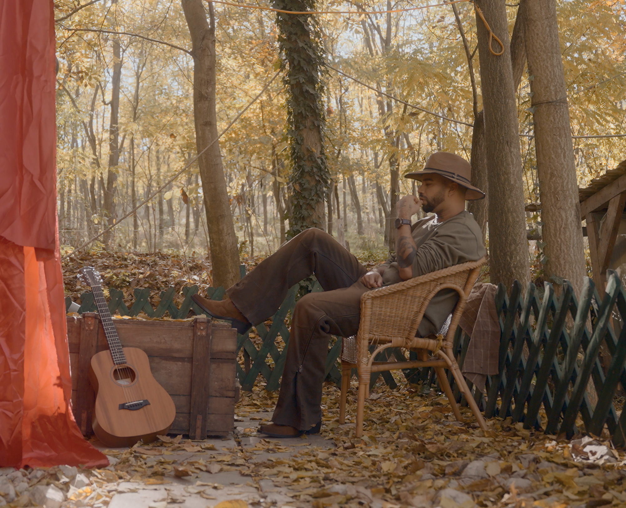 Kállay Saunders in a cowboy hat seated in an autumn forest beside an acoustic guitar, photographed for Gala Greece