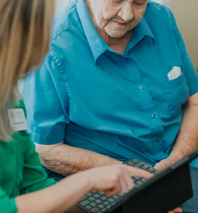 Elderly person and caregiver reviewing information on a tablet together.