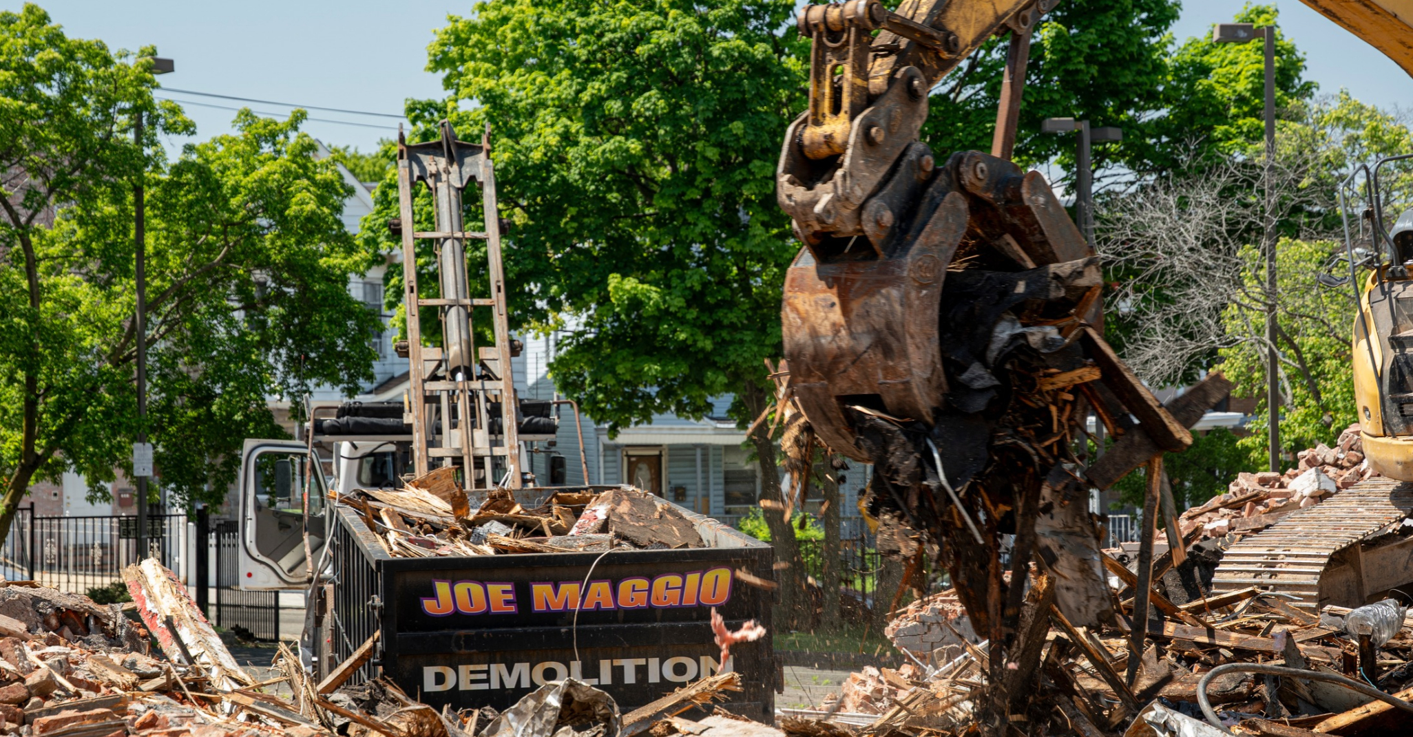 Joe Maggio Construction excavator loading demolition debris into company roll-off containers during a controlled demolition project in Jersey City, New Jersey.