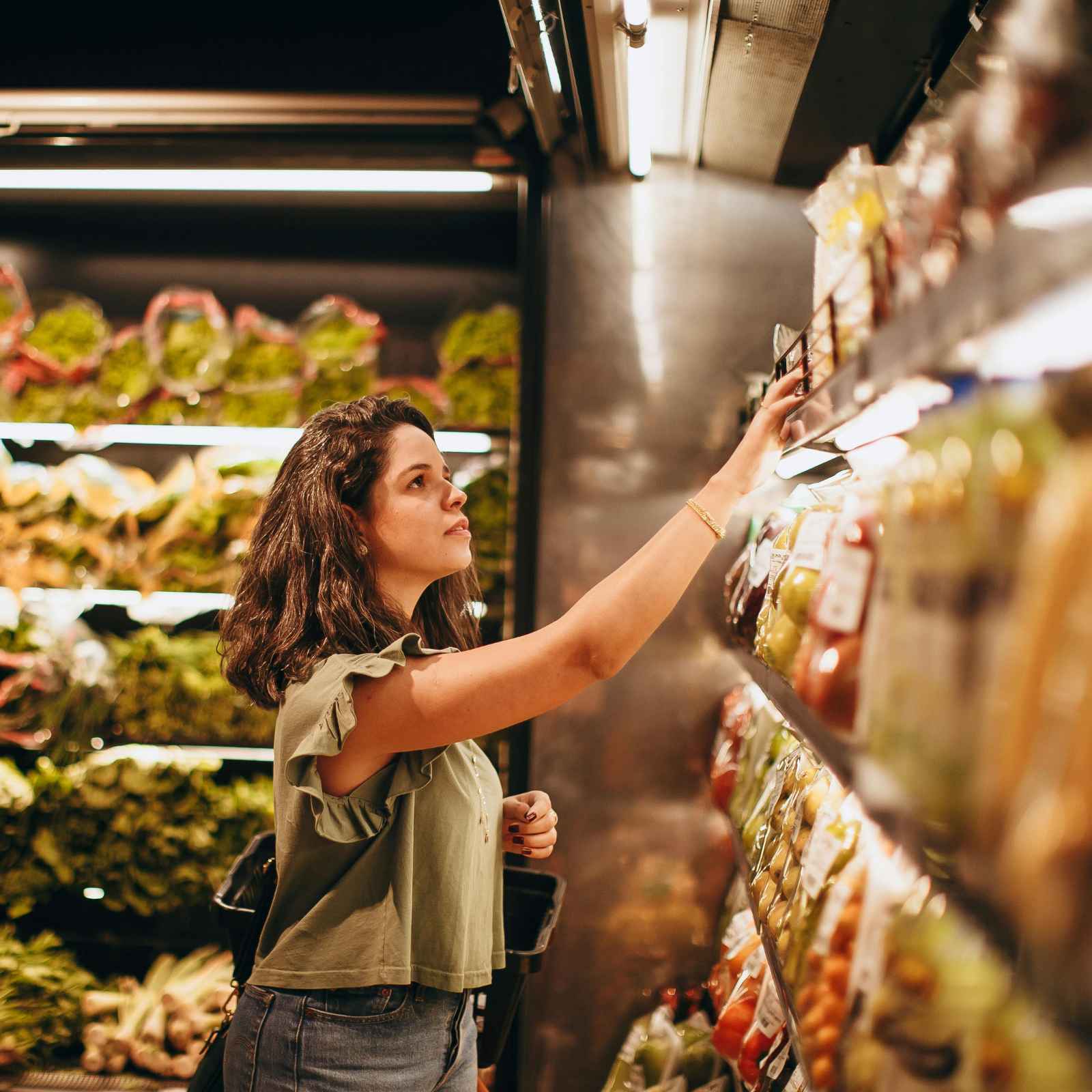 A woman reaching for a product on a well-stocked supermarket shelf