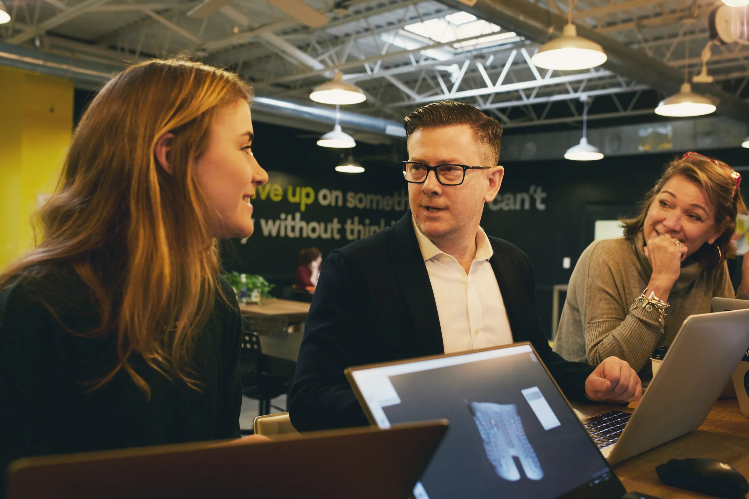 Three colleagues laughing together at their laptops