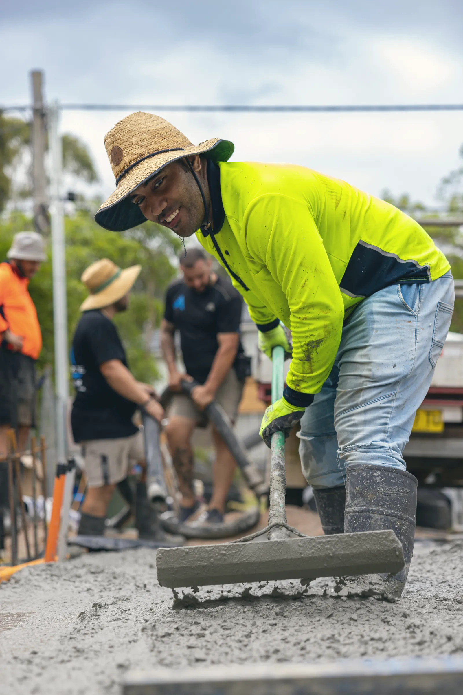 Smiling worker in hi-vis spreading concrete on site