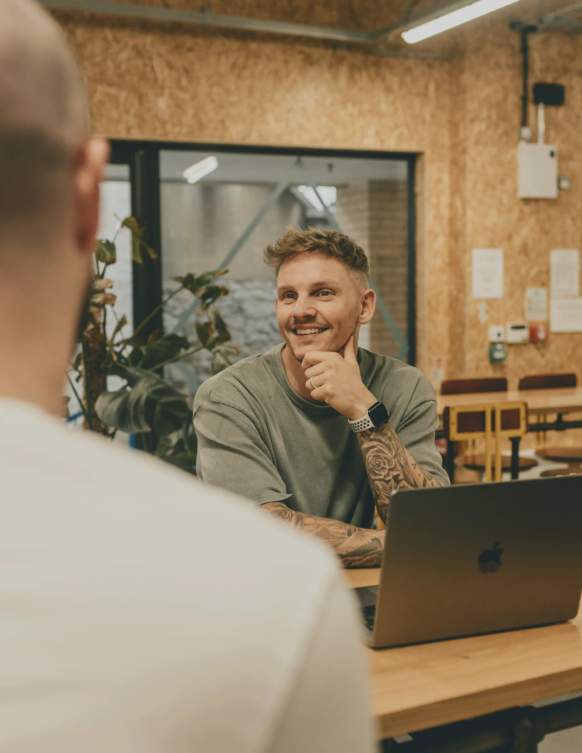 Man smiling at a colleague across a desk with a laptop