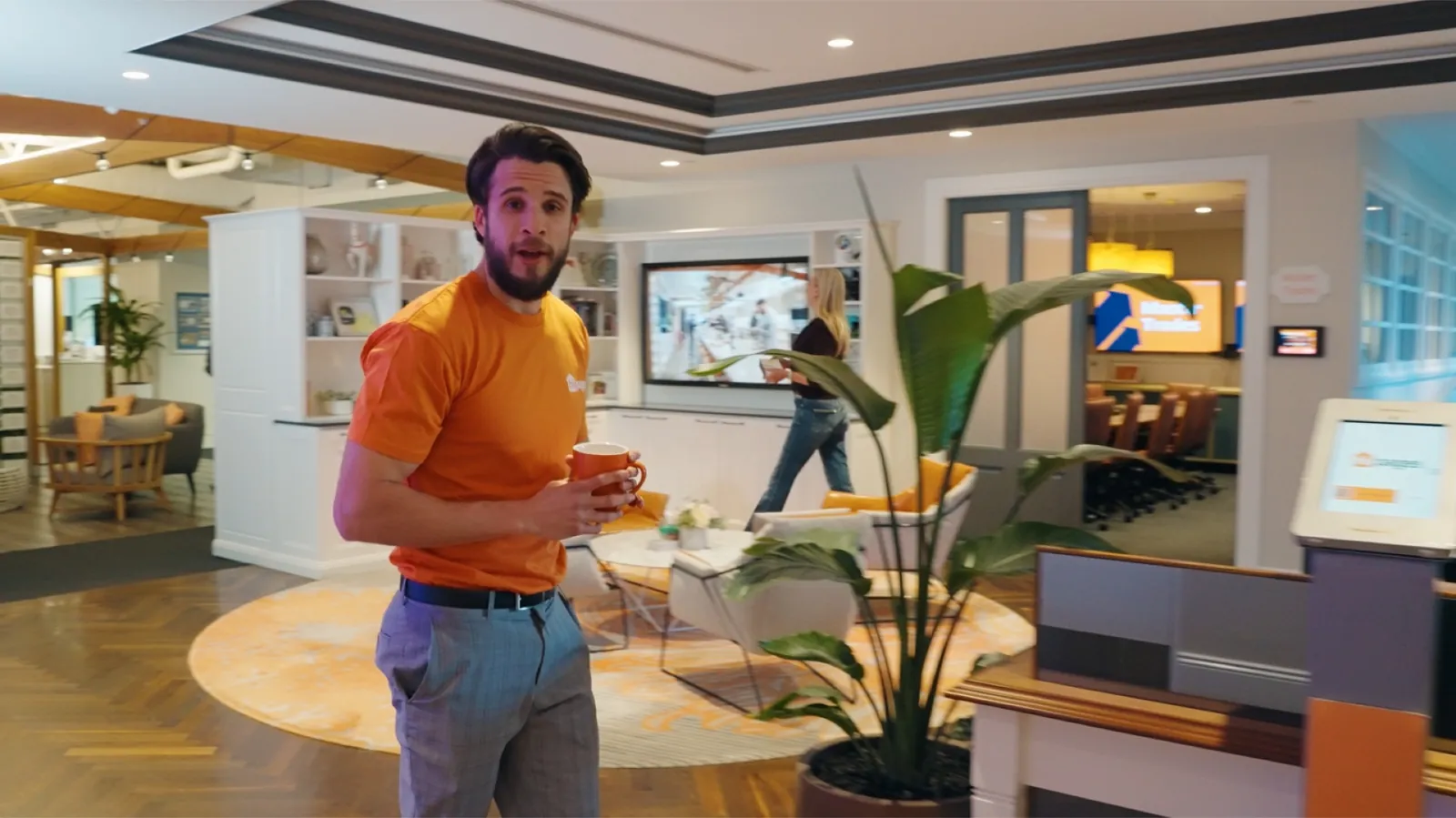 A hipages employee in an orange shirt holding a mug in the office