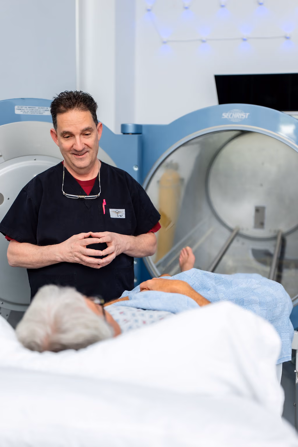 A NeuroBridge clinician beside a patient resting in a hyperbaric oxygen chamber