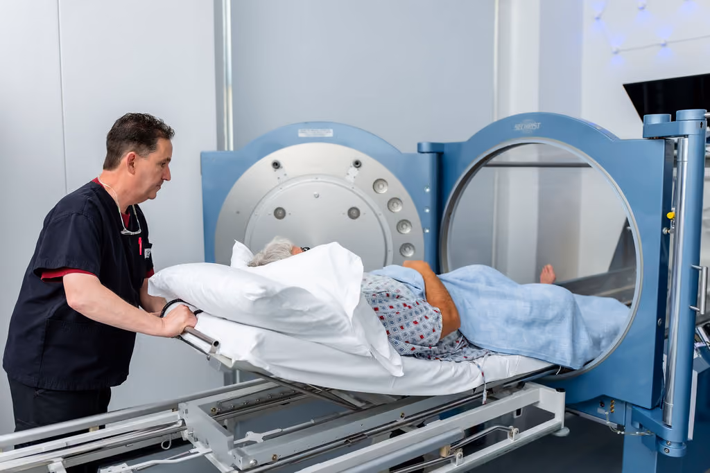 A NeuroBridge clinician helps a patient on a stretcher into the hyperbaric oxygen chamber