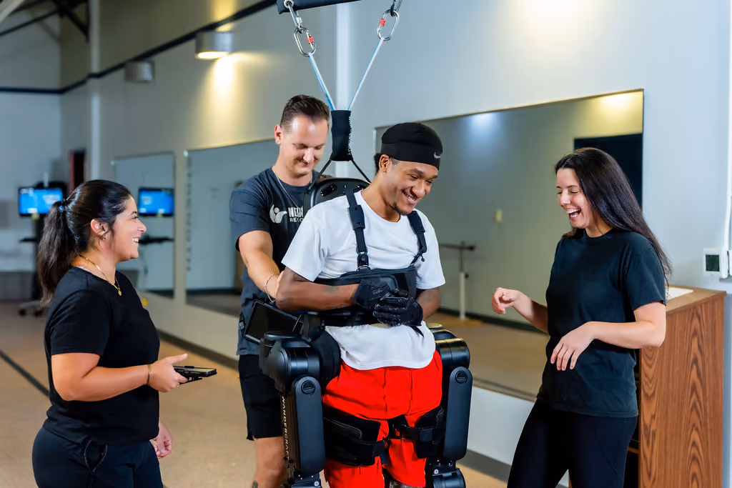 NeuroBridge clinicians supporting a smiling patient in a robotic gait trainer