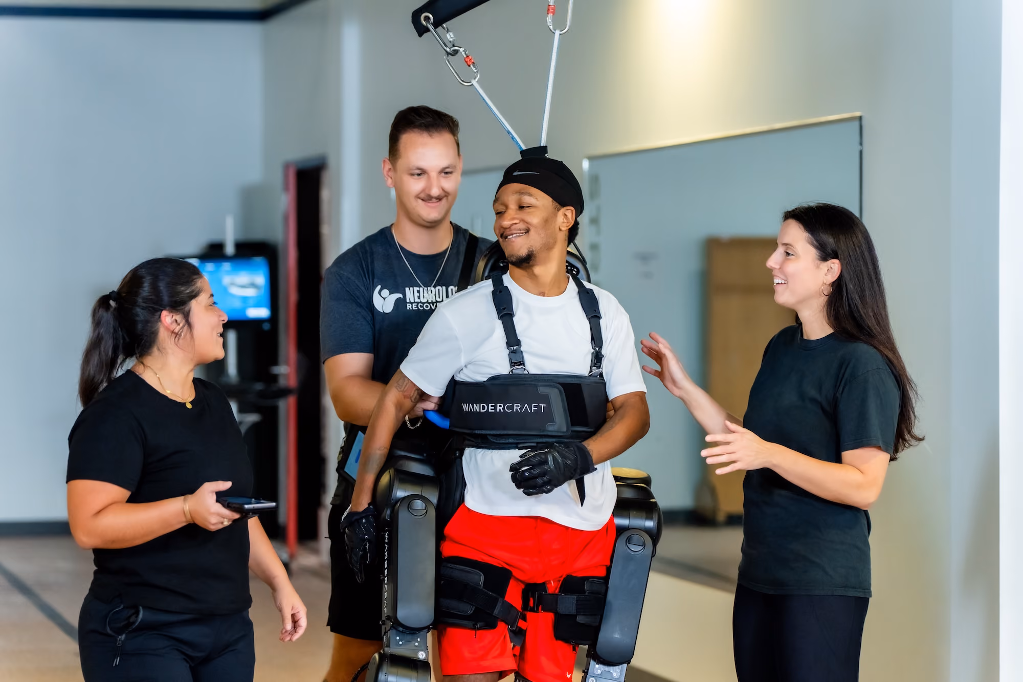 A patient walks in a robotic exoskeleton, supported and encouraged by three NeuroBridge clinicians