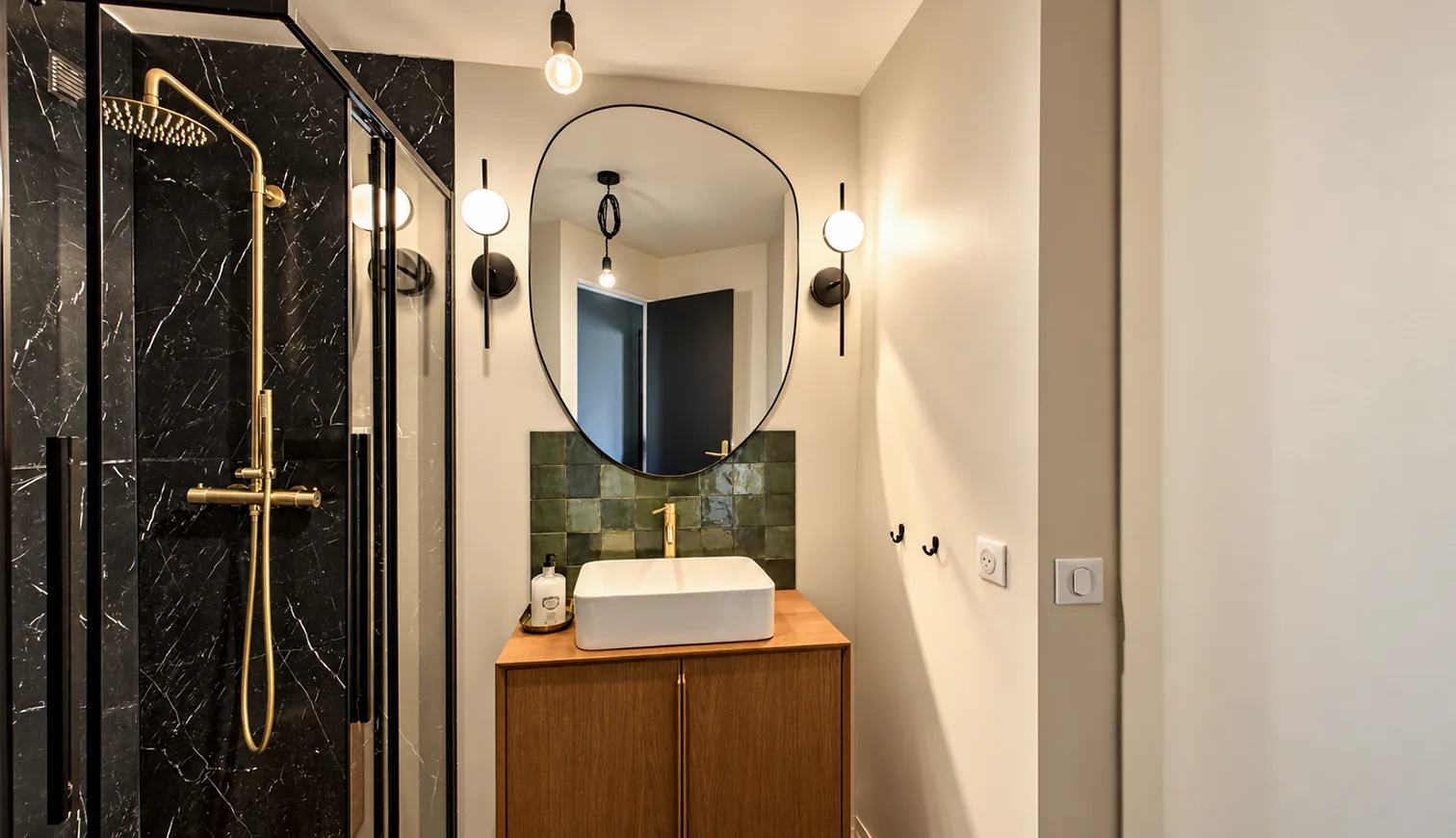 Salle d'eau avec douche en marbre noir, robinetterie dorée, vasque blanche et miroir rond.
