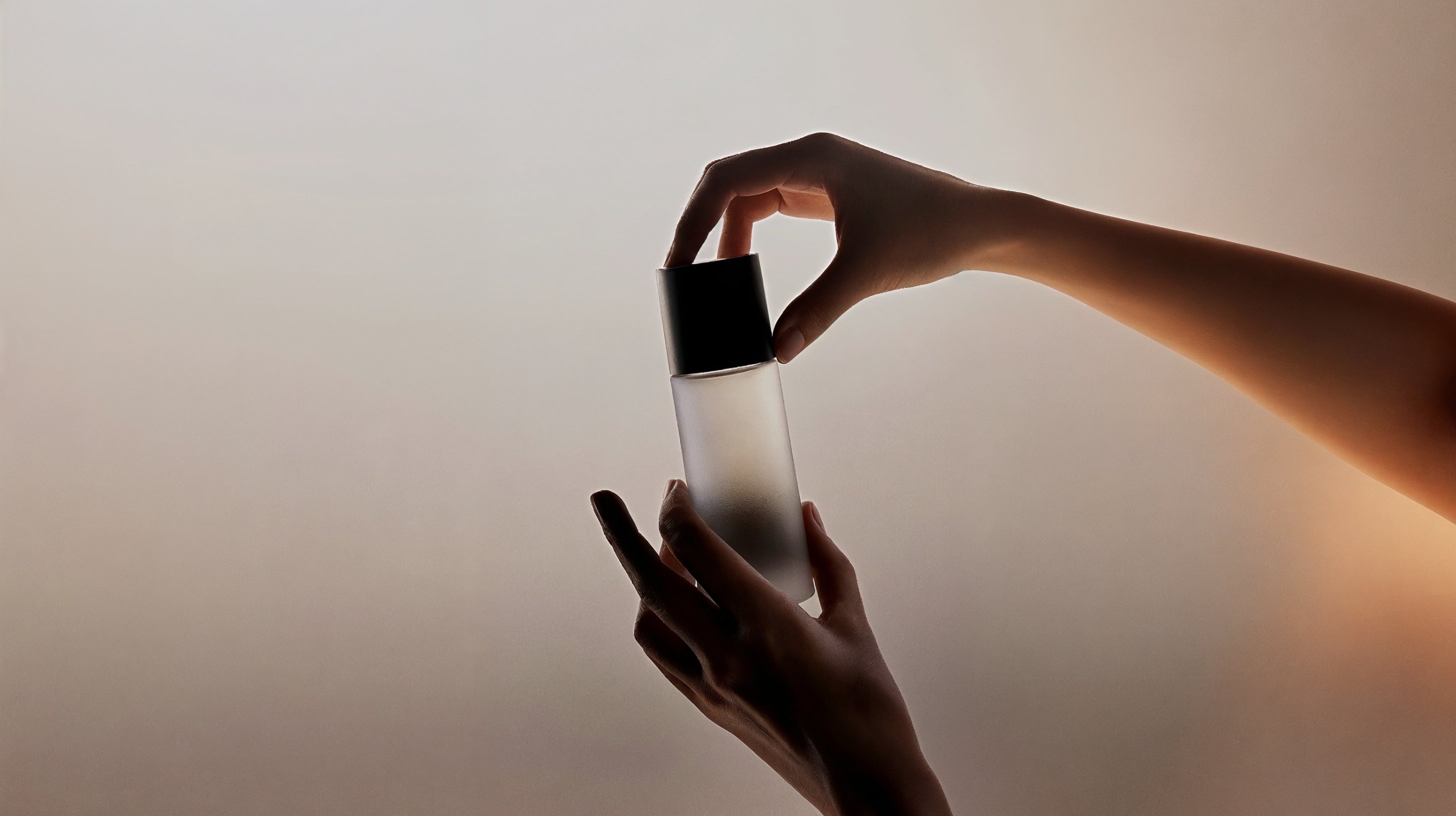 Hands holding a frosted glass bottle with a black cap against a neutral background.