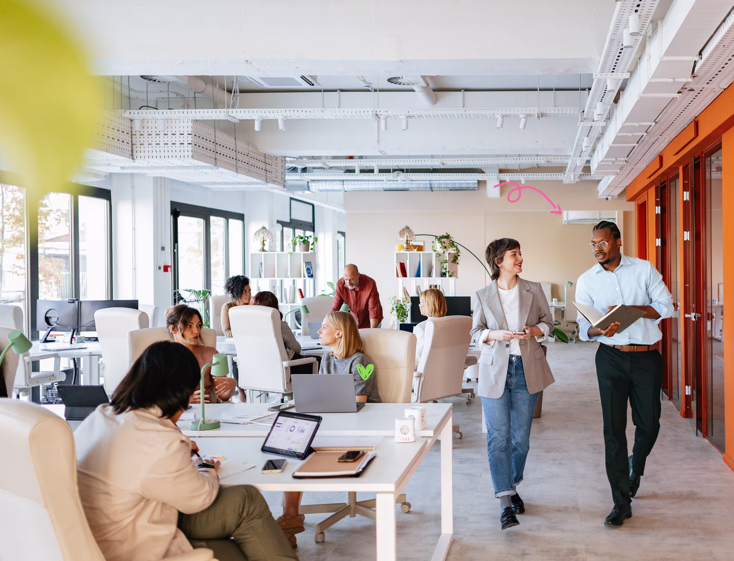 Modern open office with diverse colleagues working at desks and two people talking beside a window.