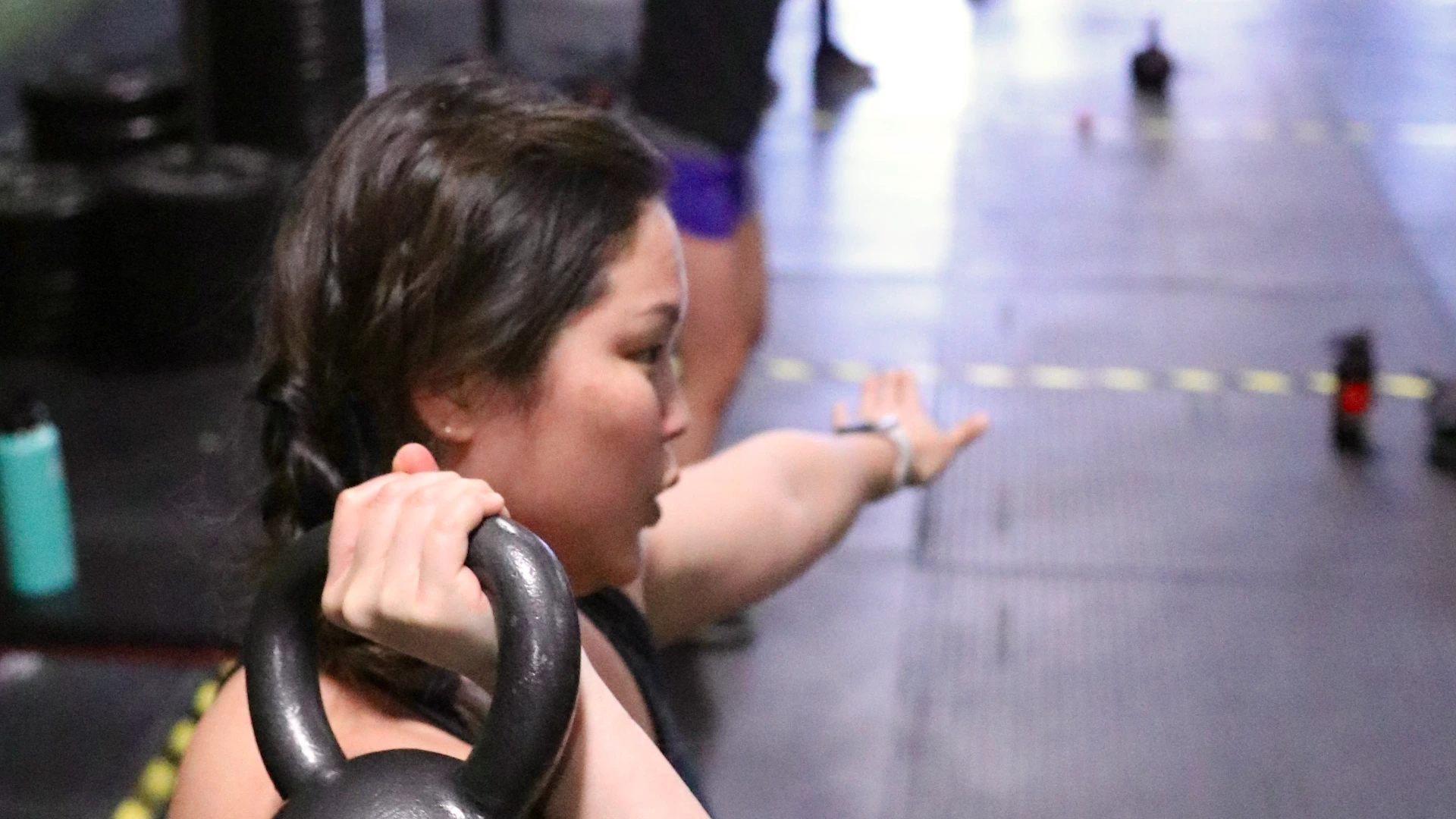 A woman holds a kettlebell in a rack position during a group gym workout.