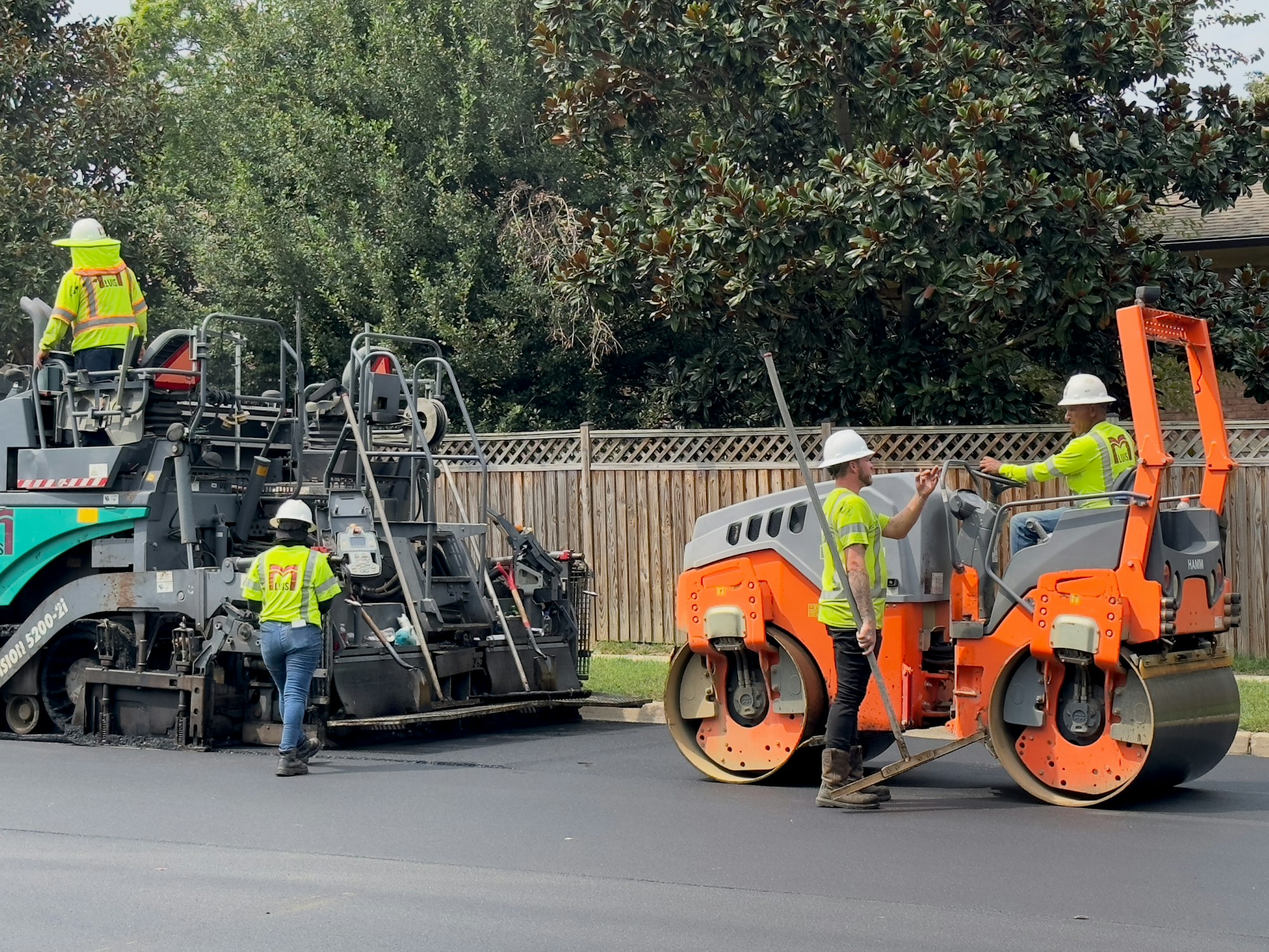 Paving crew in hi-vis vests laying and rolling new asphalt