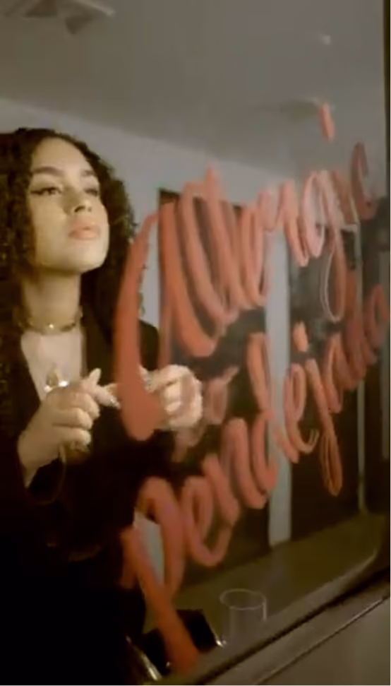 A woman with curly hair and dark clothing is writing on a glass surface with red marker; the writing is cursive but not fully legible.