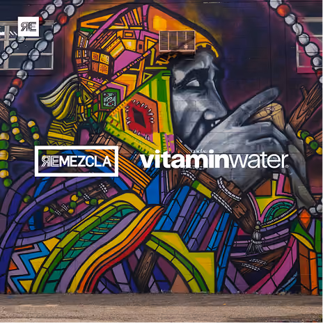 Colorful mural of a person with vibrant geometric patterns on the face and clothing, holding a microphone near the mouth, with logos for ReMezcla and vitaminwater overlaid on the mural.