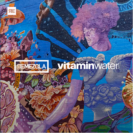 Colorful mural featuring a large purple-toned figure with an afro holding a golden eagle, surrounded by detailed flowers, abstract shapes, and cosmic elements, with logos for 'REMEZCLA' and 'vitaminwater' overlayed in white text.