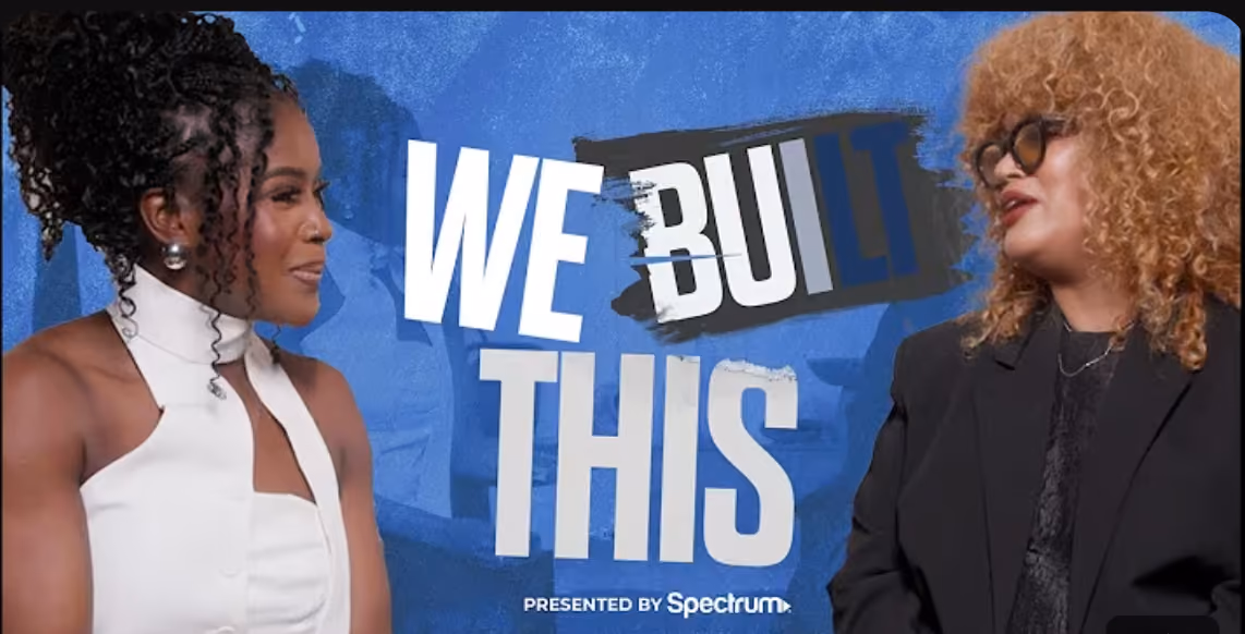 Two women facing each other against a blue background with large text 'WE BUILT THIS' and smaller text 'PRESENTED BY Spectrum'. The woman on the left has curly black hair and wears a white sleeveless top, and the woman on the right has curly blonde hair, glasses, and wears a black outfit.