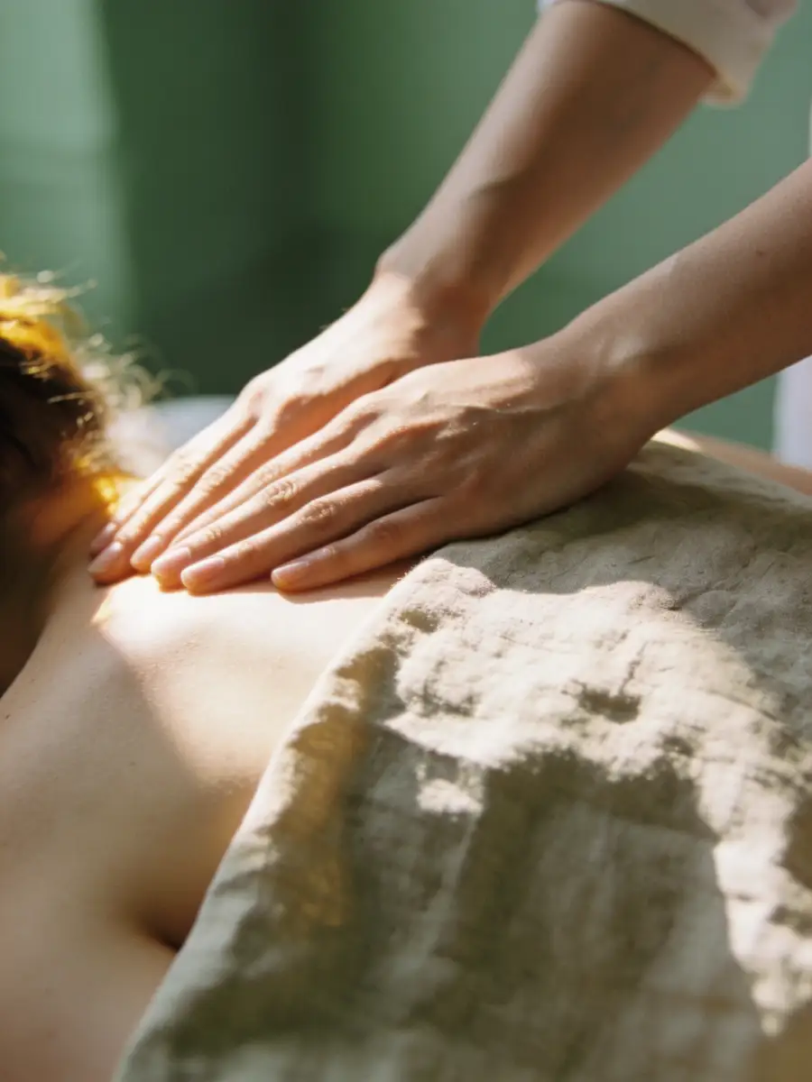 Person receiving a relaxing back massage with sunlight casting soft shadows, covered partially by a light beige towel.