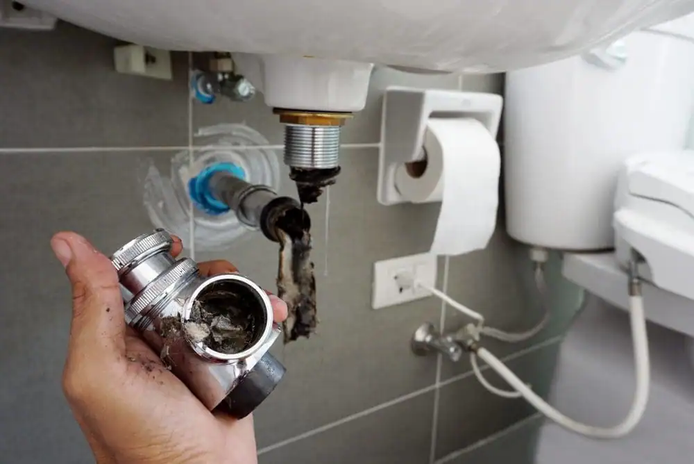 Plumber-Holding-Corroded-Sink-Drain-Fitting-Removed-From-Bathroom-Sink
