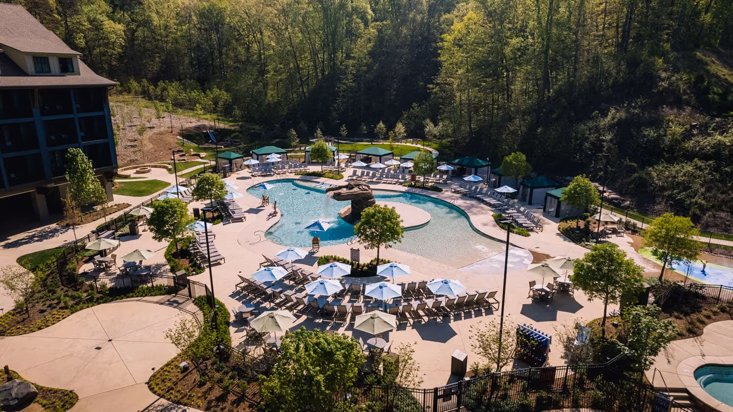 Resort-style outdoor pool area with lounge chairs and umbrellas surrounded by trees, D&S Builders hospitality construction