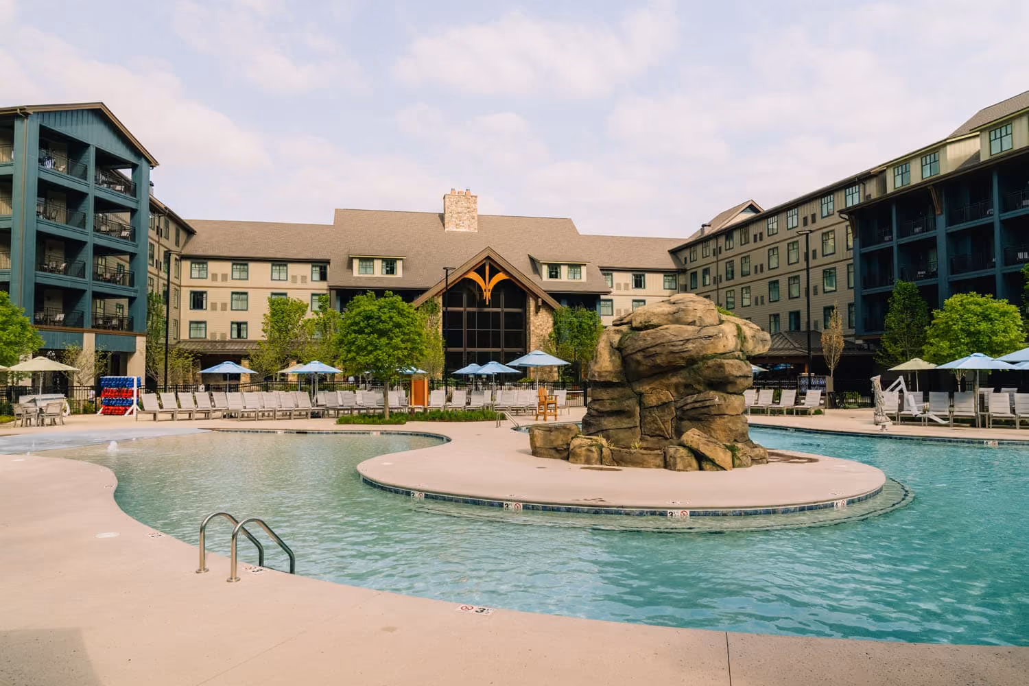 Hospitality resort pool courtyard with a rock feature, surrounded by multi-story buildings and lounge chairs