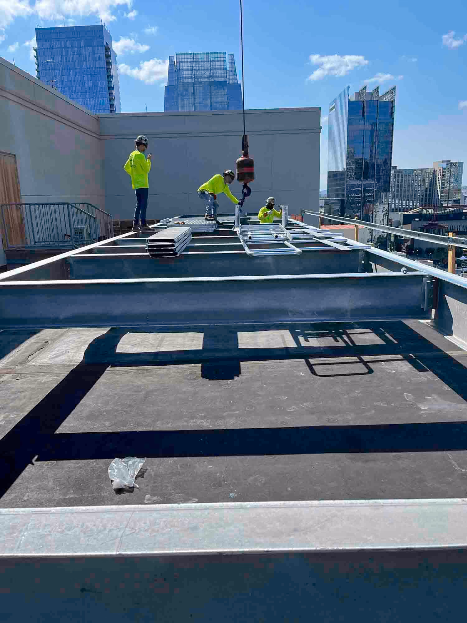 Workers assembling steel framing on a rooftop construction site with city buildings in the background.