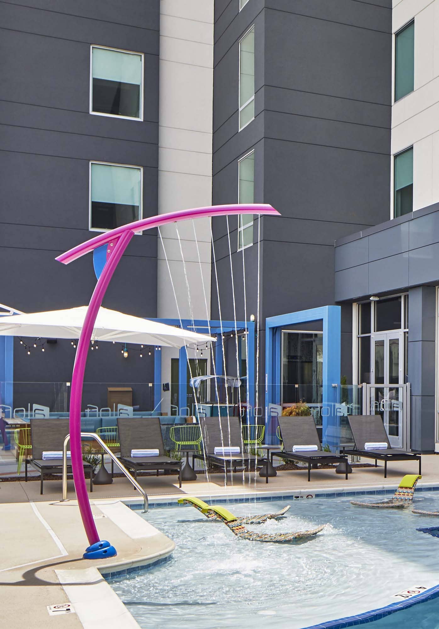 Modern hotel pool with colorful water feature and lounge chairs, D&S Builders hospitality construction