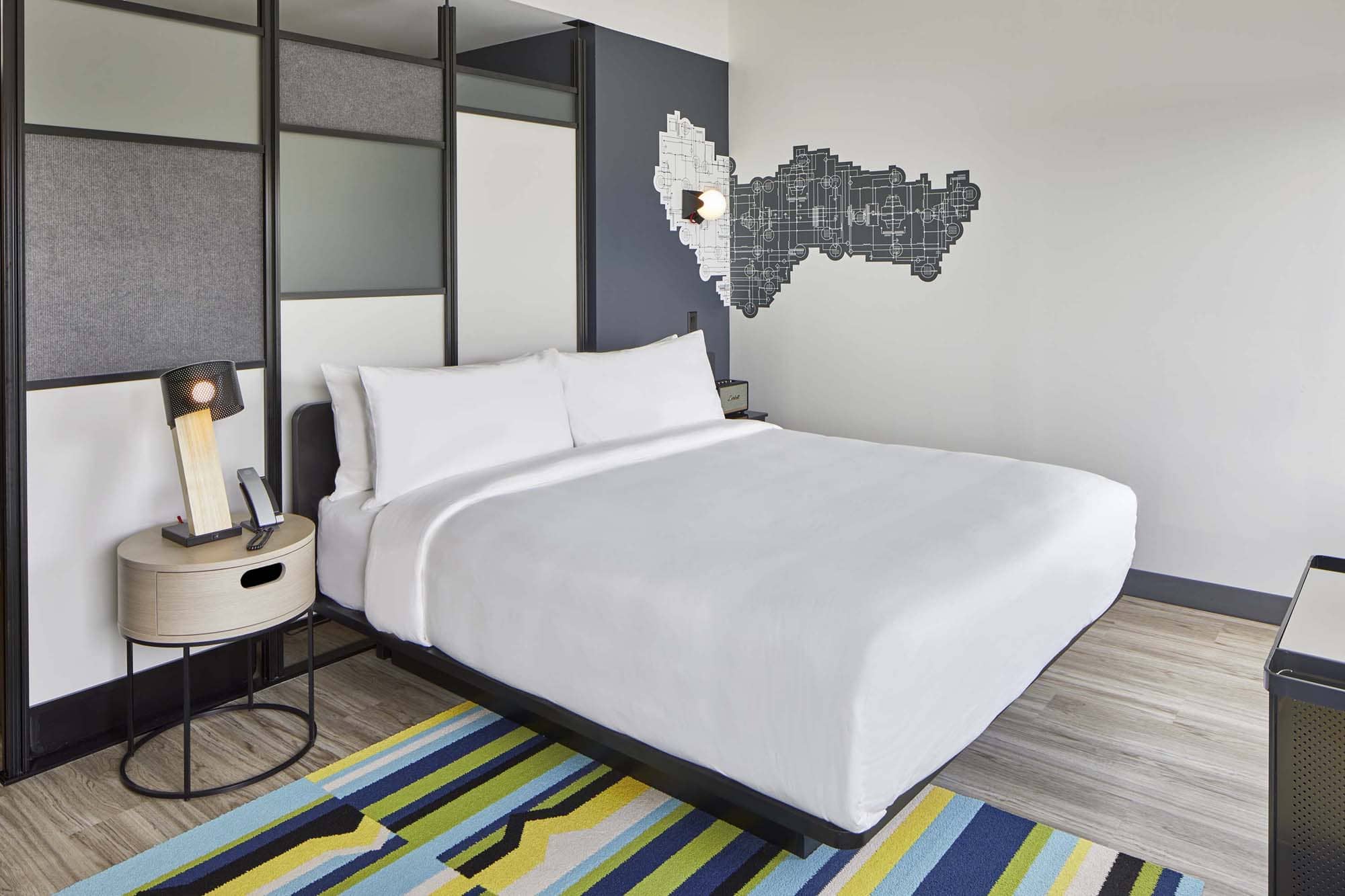 Modern hotel room with a bed, bedside lamp, and colorful rug, likely for hospitality construction by D&S Builders