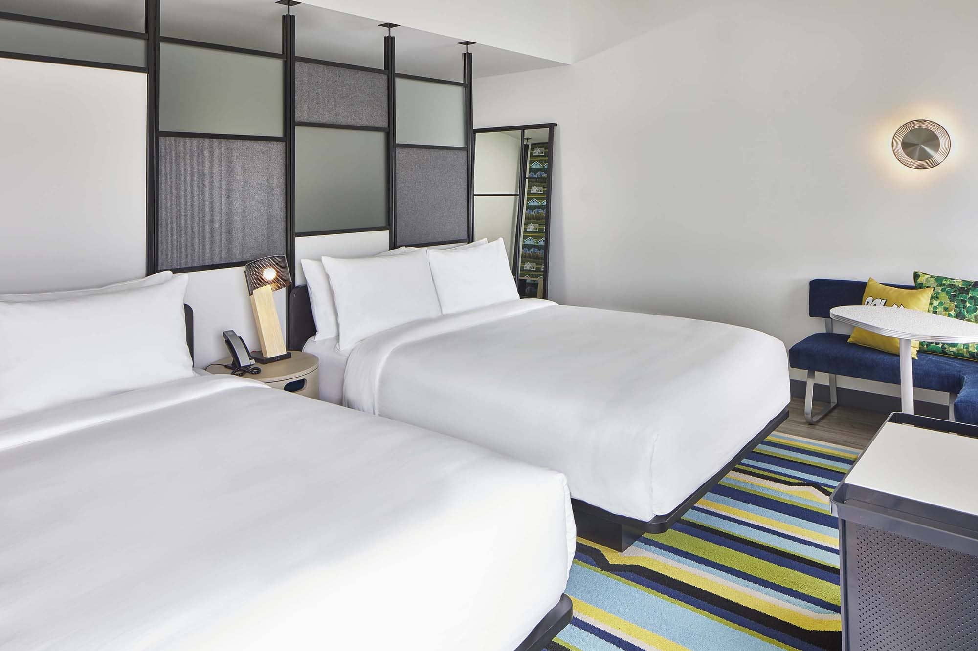 Modern hotel room with two beds, colorful striped rug, and seating area