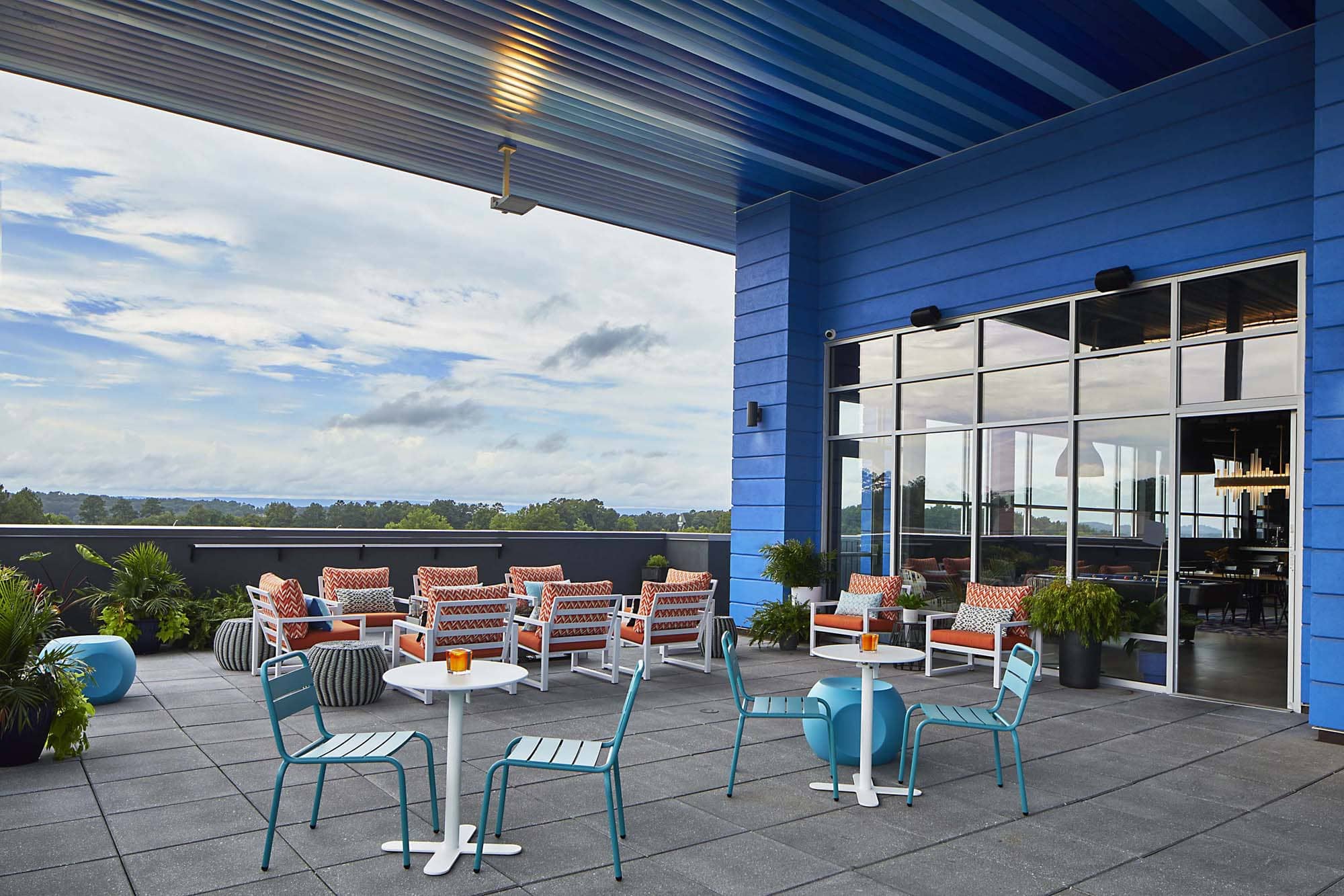 Rooftop hospitality patio with seating beside a blue building and glass doors