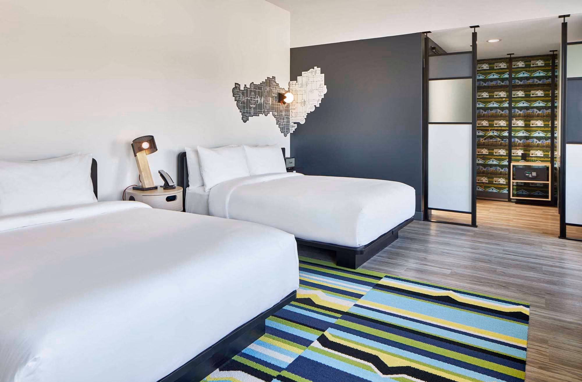 Modern hotel room with two beds, striped rug, and map wall art