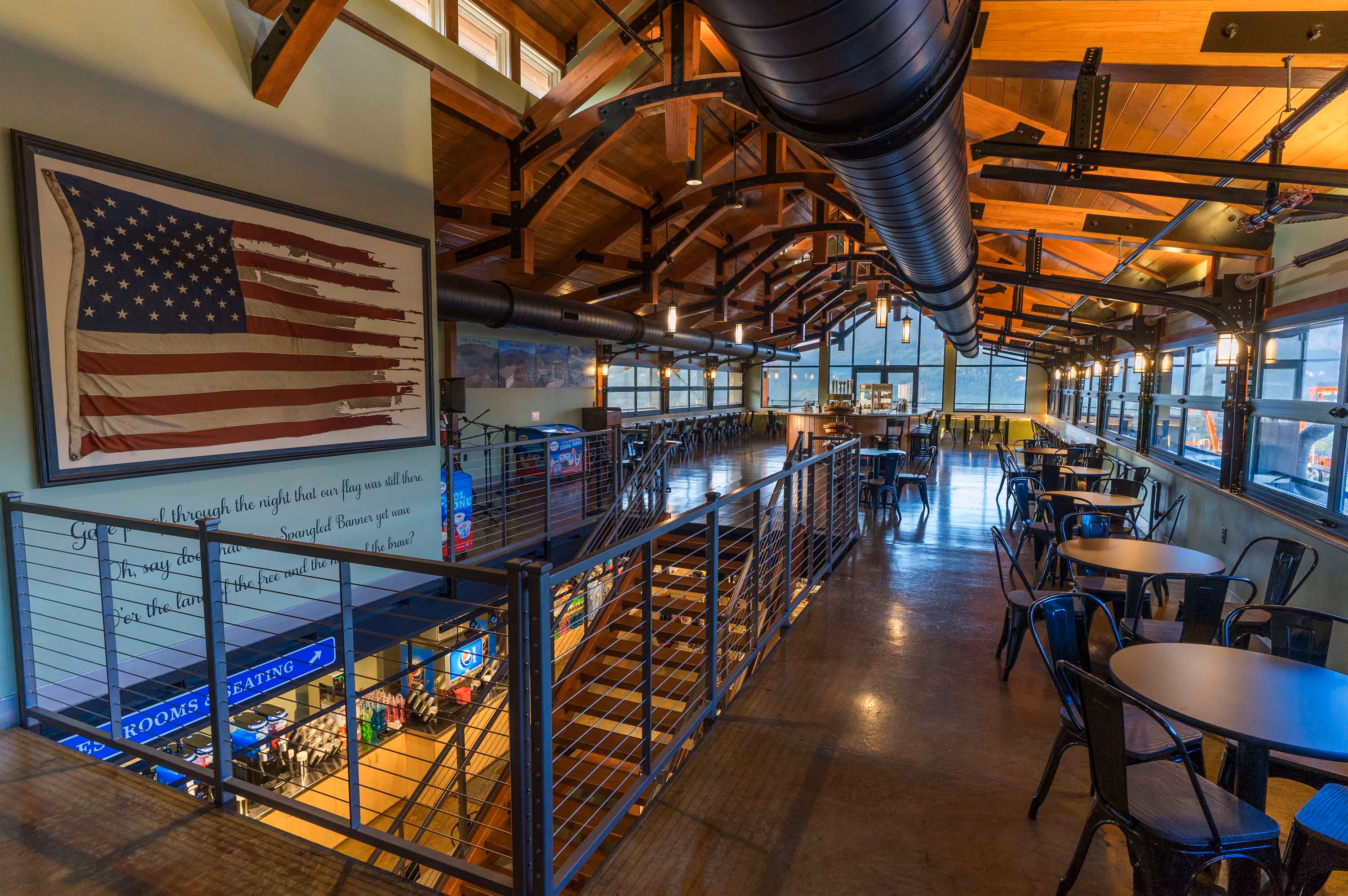 Rustic restaurant mezzanine with tables, exposed beams, and a large American flag wall display
