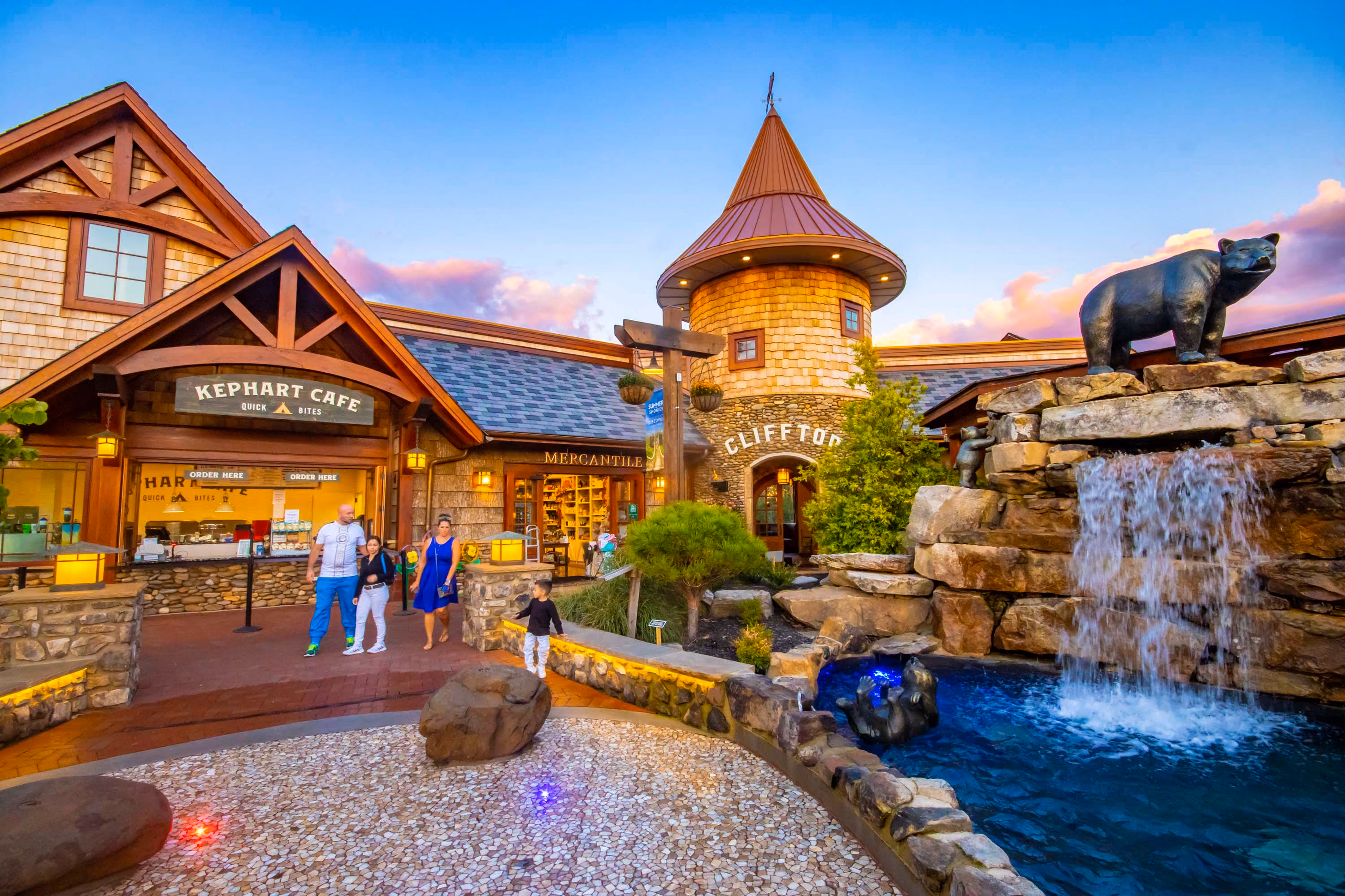 Hospitality construction at Clifton with a stone waterfall, bear statue, and café entrance at dusk