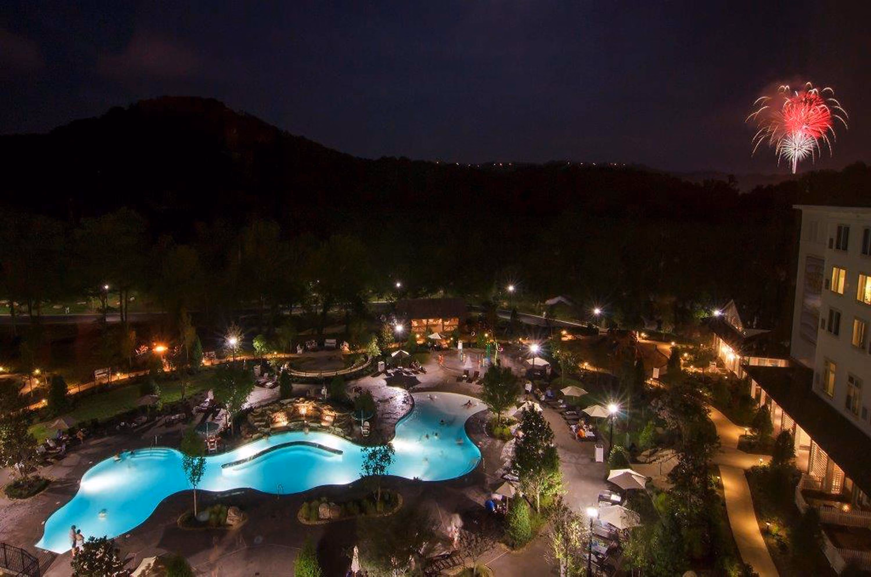 Nighttime resort pool area with fireworks over the mountains, likely in Gatlinburg