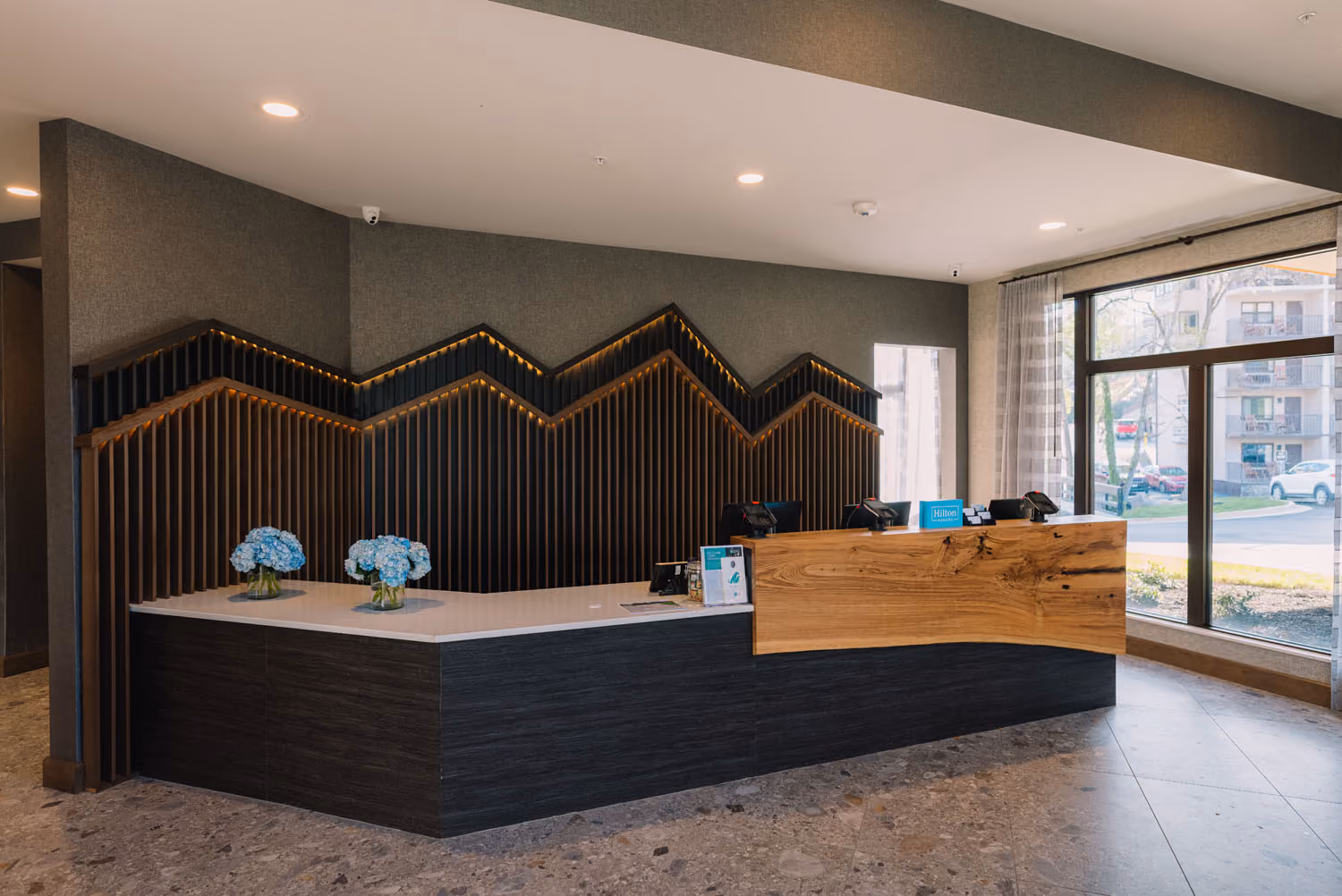 Modern hotel lobby reception desk with wood accents and large windows