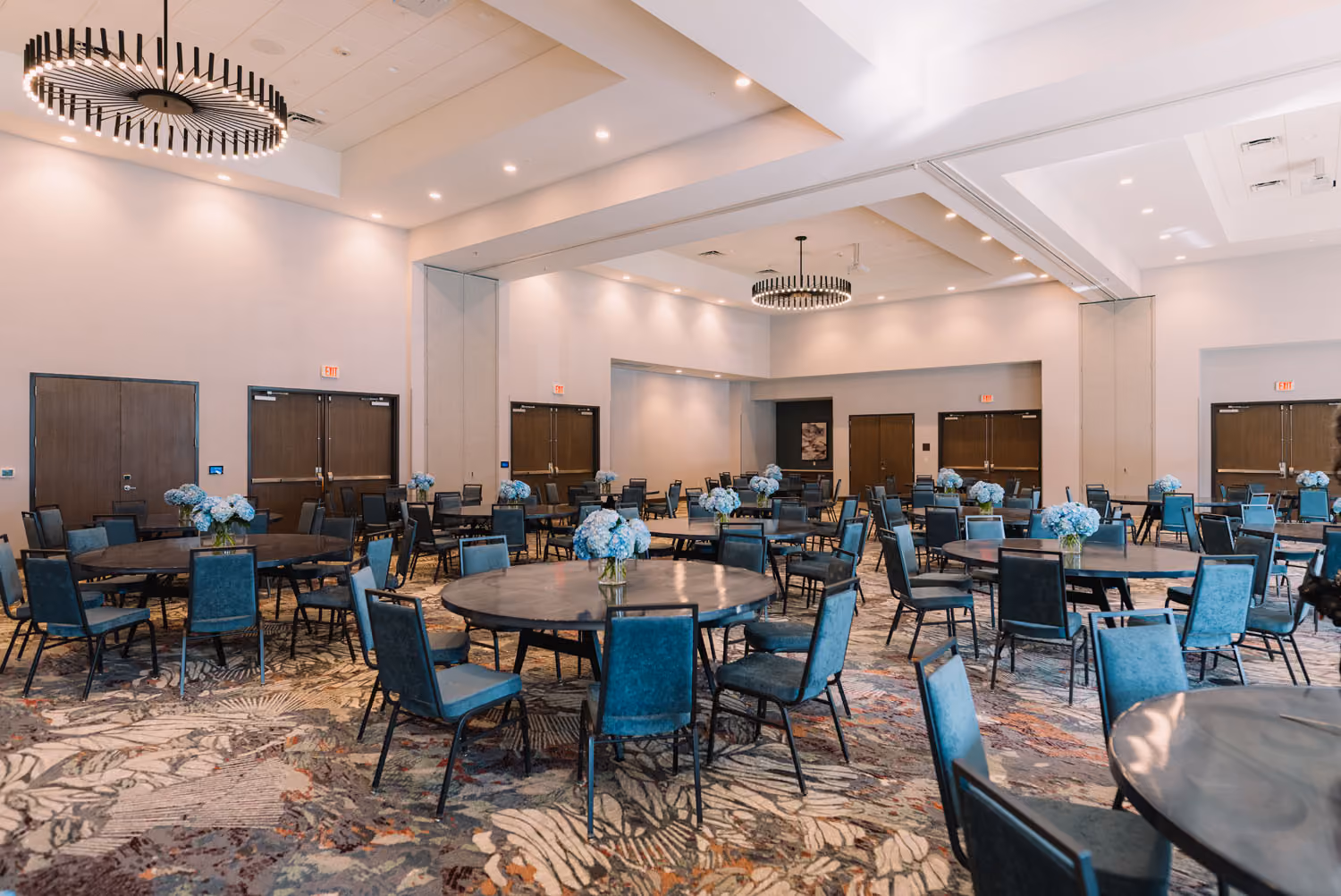 Spacious hospitality event hall with round tables, blue chairs, and modern chandeliers