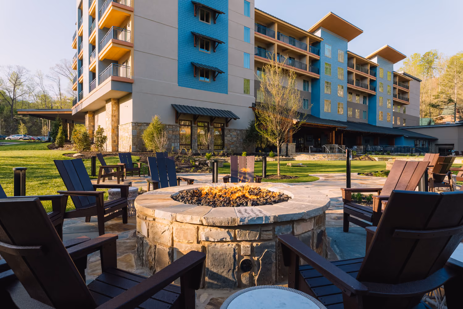 Hotel courtyard with fire pit and Adirondack chairs outside a modern building