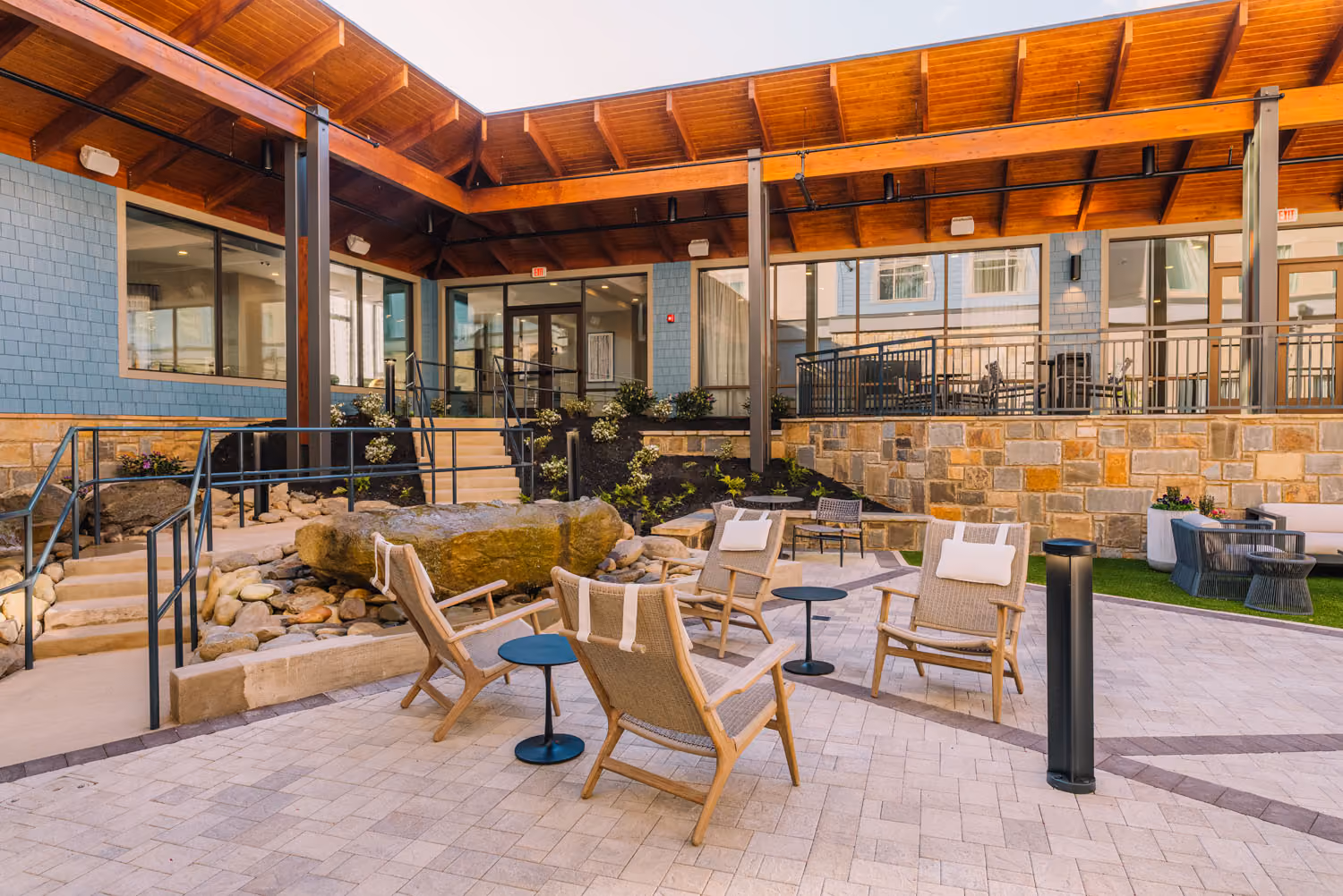 Covered hospitality courtyard with seating, stone landscaping, and wood-beam roof by D&S Builders