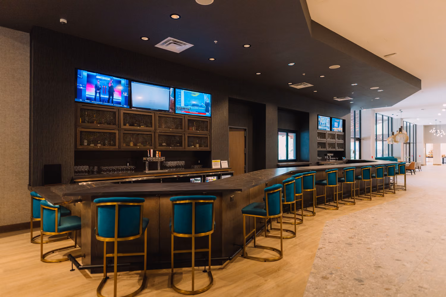 Modern hotel bar with teal stools and wall-mounted TVs