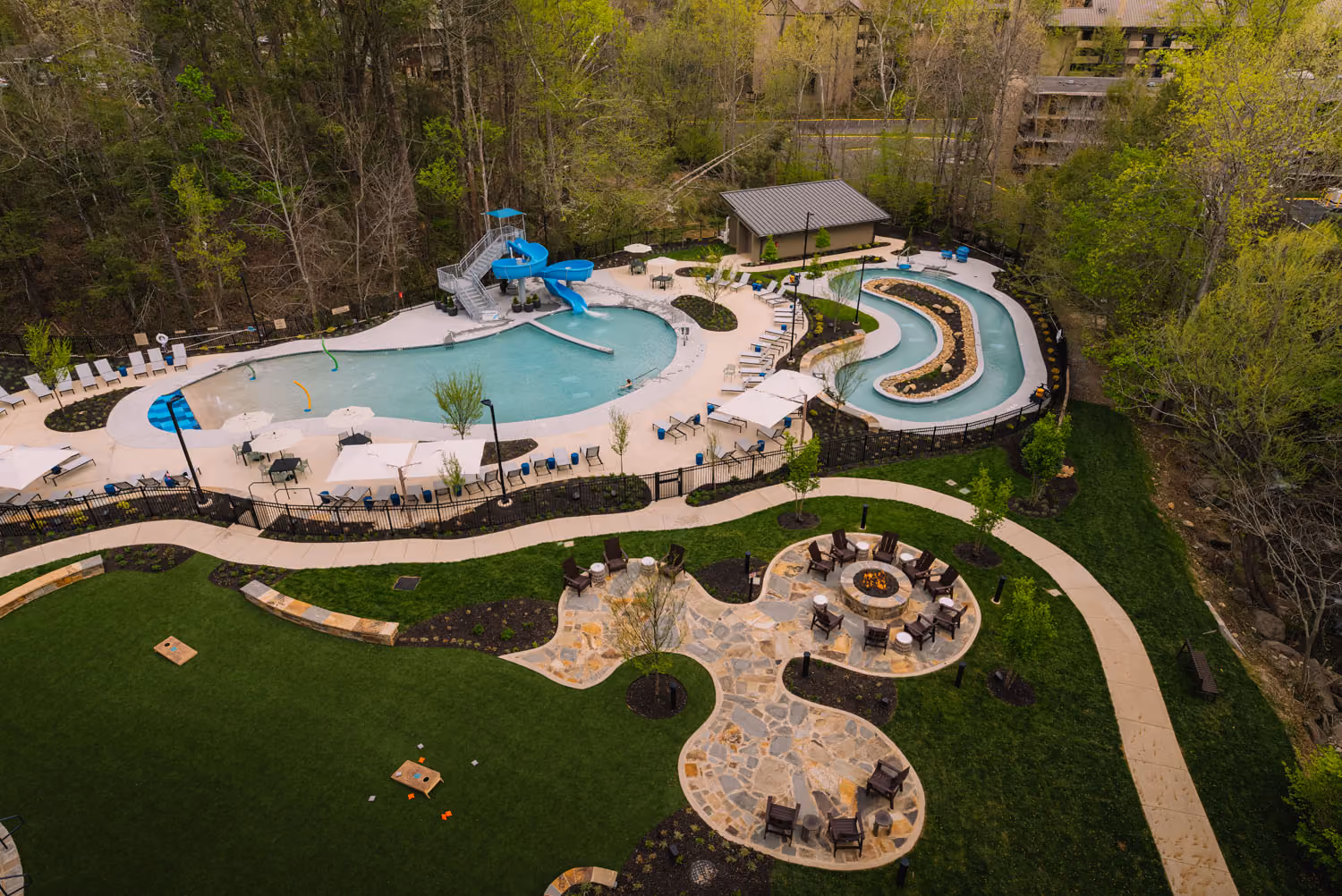 Aerial view of a resort-style pool area with water slides, lounge chairs, and fire pits by D&S Builders