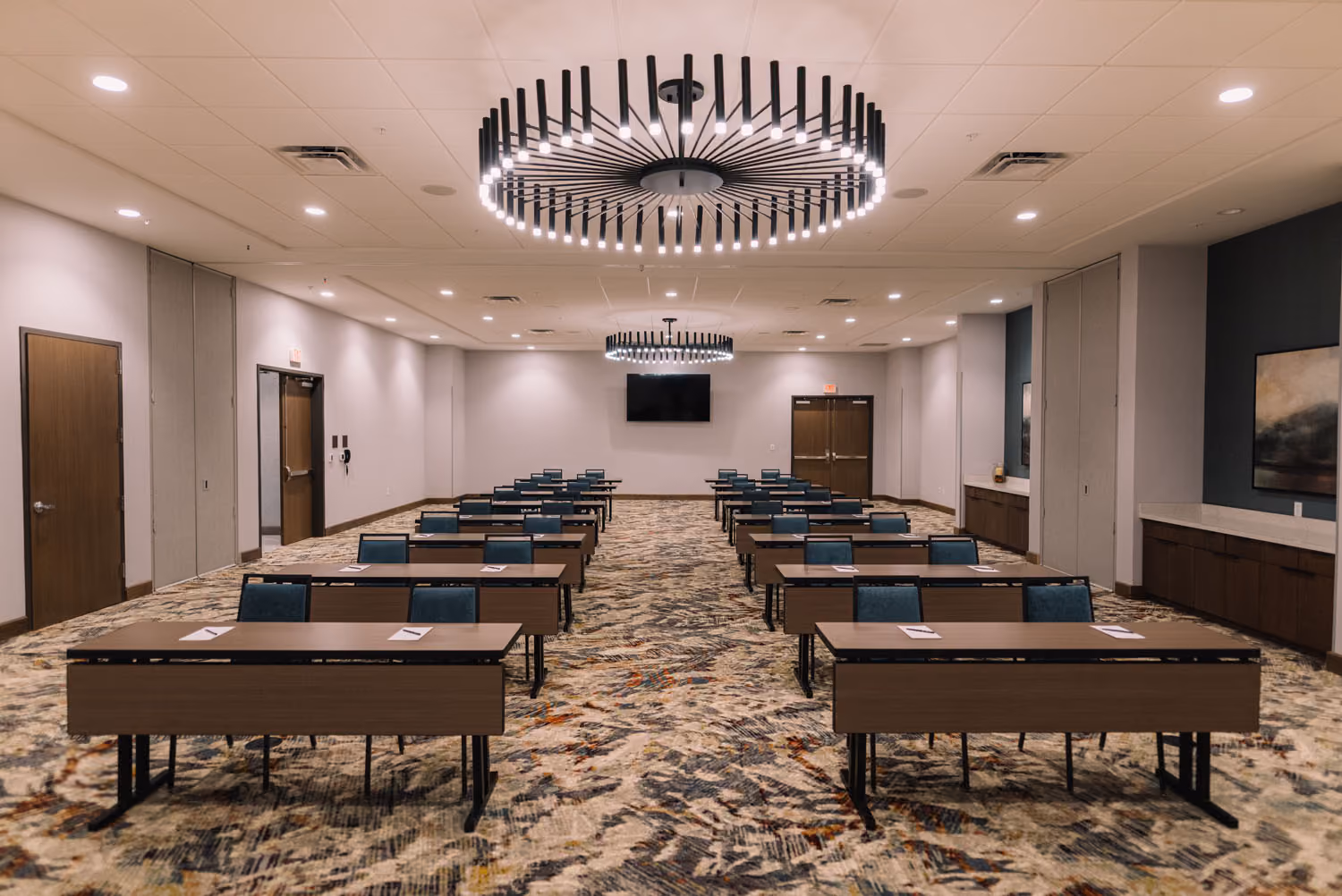 Modern conference room with rows of tables, teal chairs, and circular ceiling lights