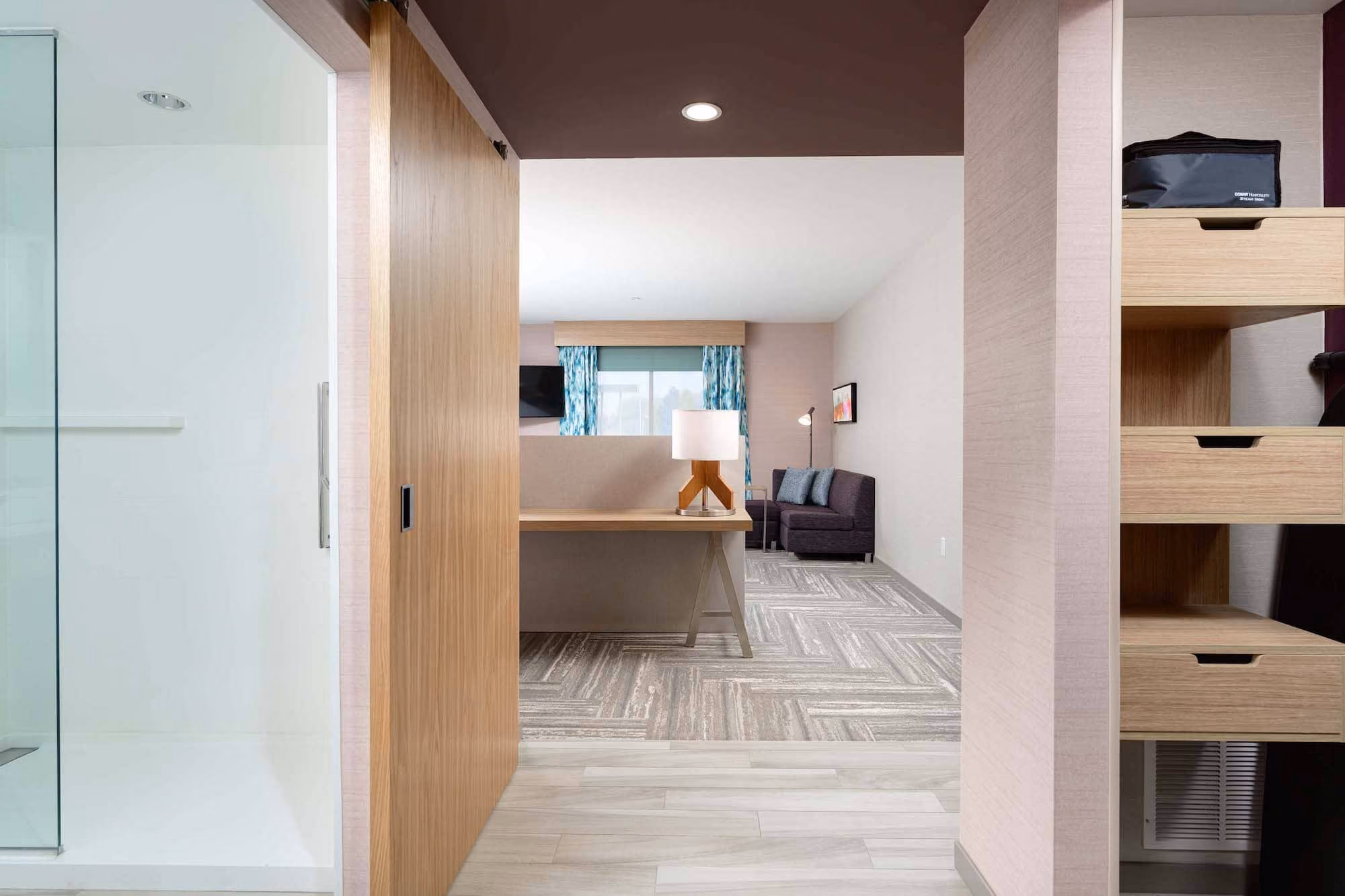 Modern hotel suite interior with desk, sofa, and bathroom entry