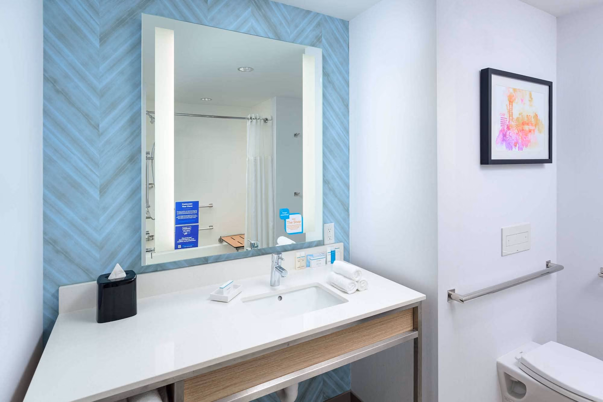 Modern hotel bathroom vanity with large mirror and blue herringbone accent wall, D&S Builders construction