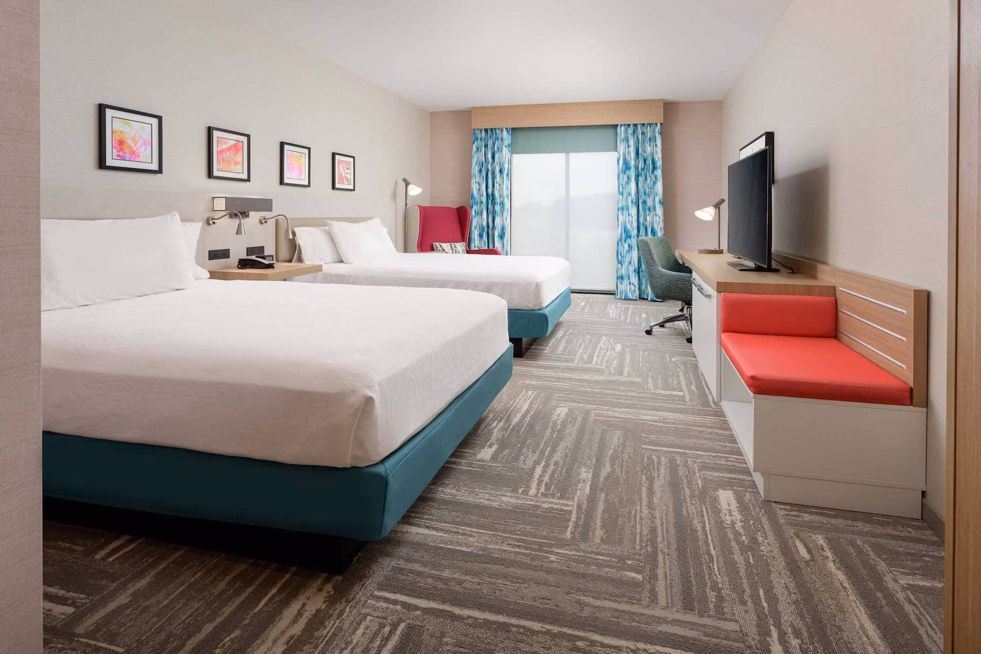 Modern hotel room with two beds, TV, and desk seating