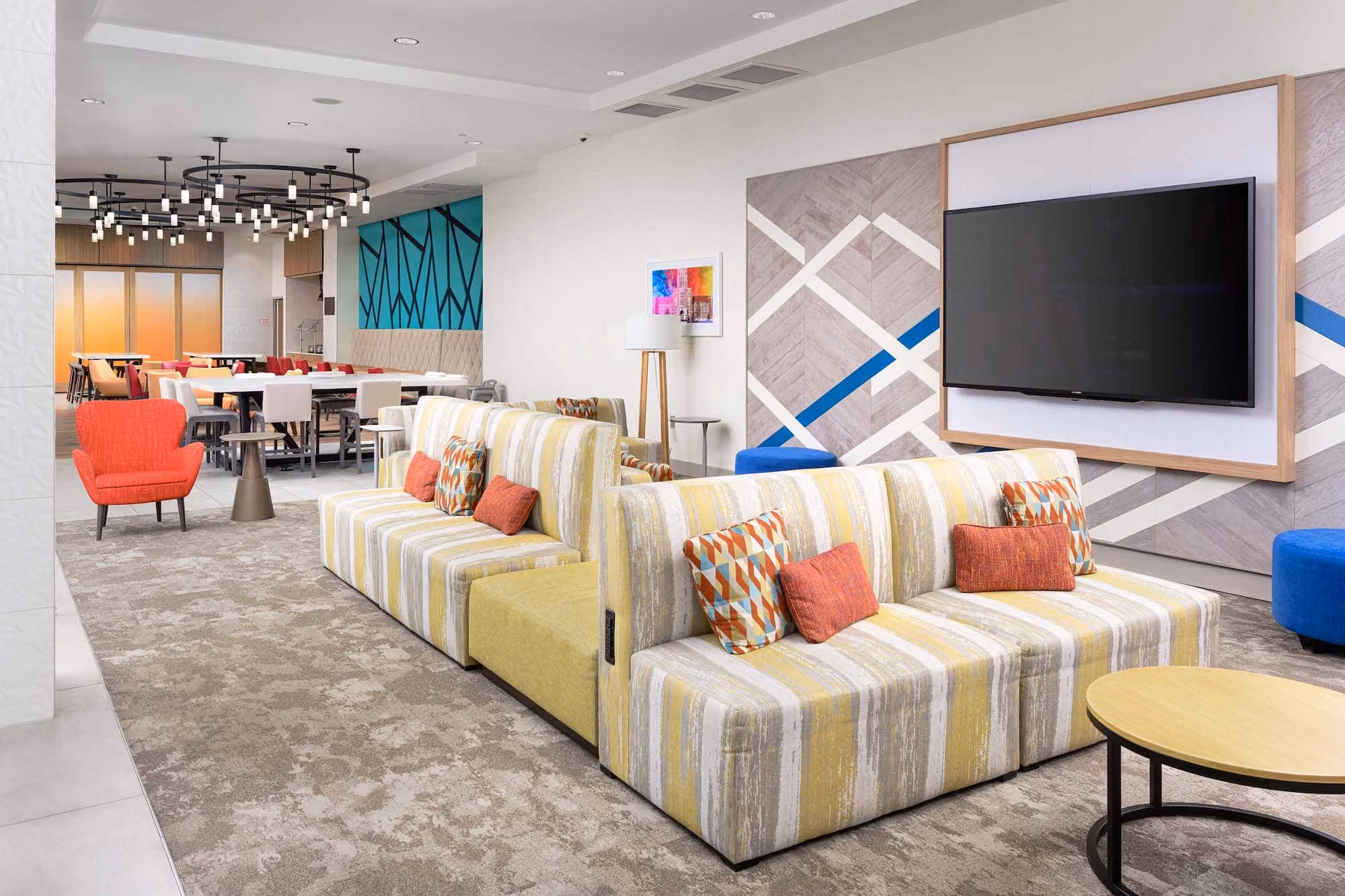 Modern hotel lounge with striped sofas, colorful chairs, and a large wall-mounted TV
