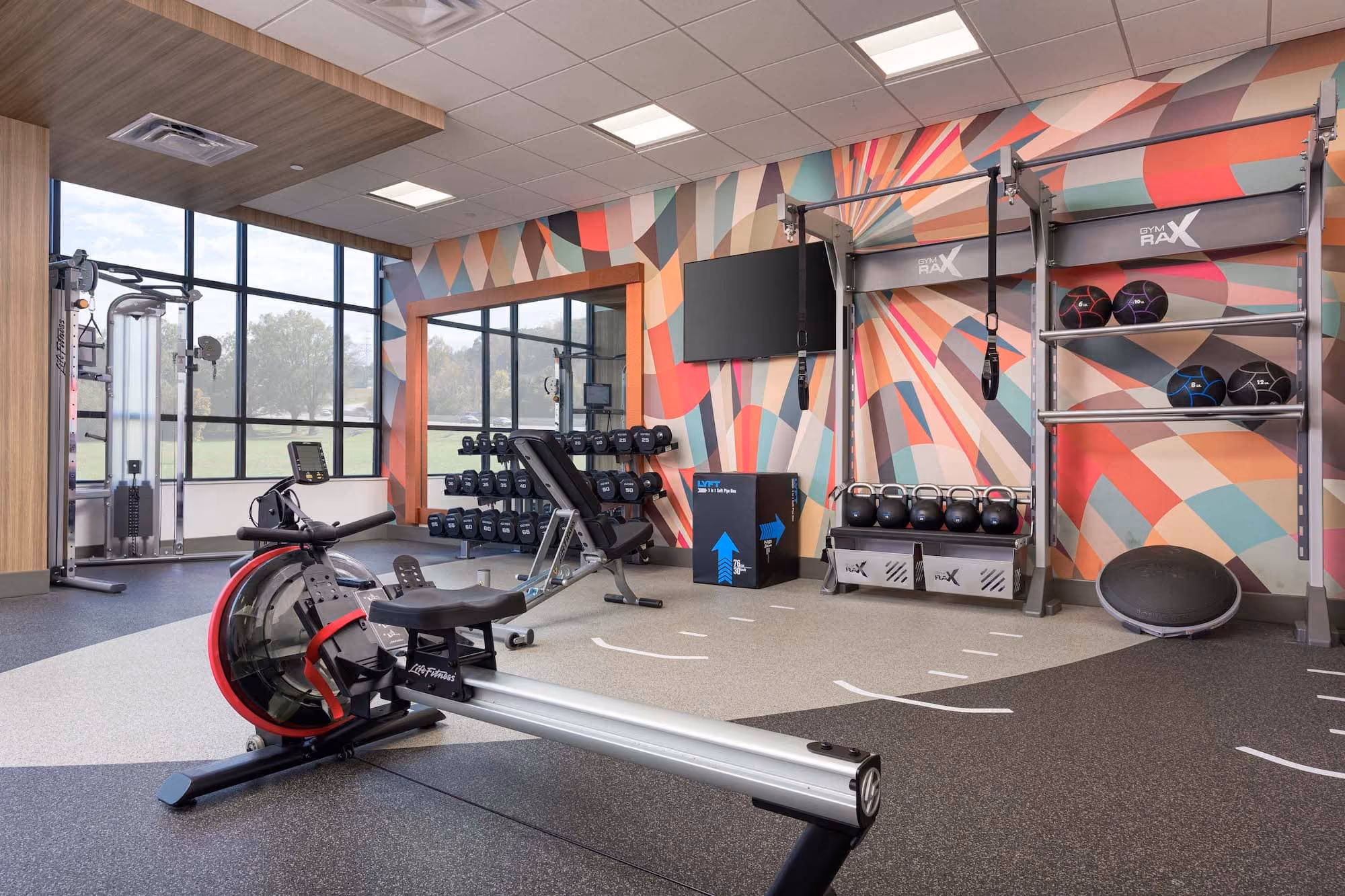 Modern gym interior with rowing machine, weights, and colorful mural wall